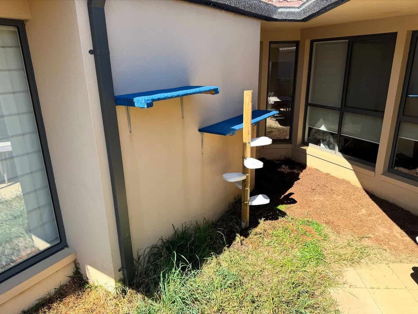 Small Outdoor Patio With Blue Shelves on a Beige Wall, a Pole With White Shelves — Catios By Paulie in Sydney, NSW