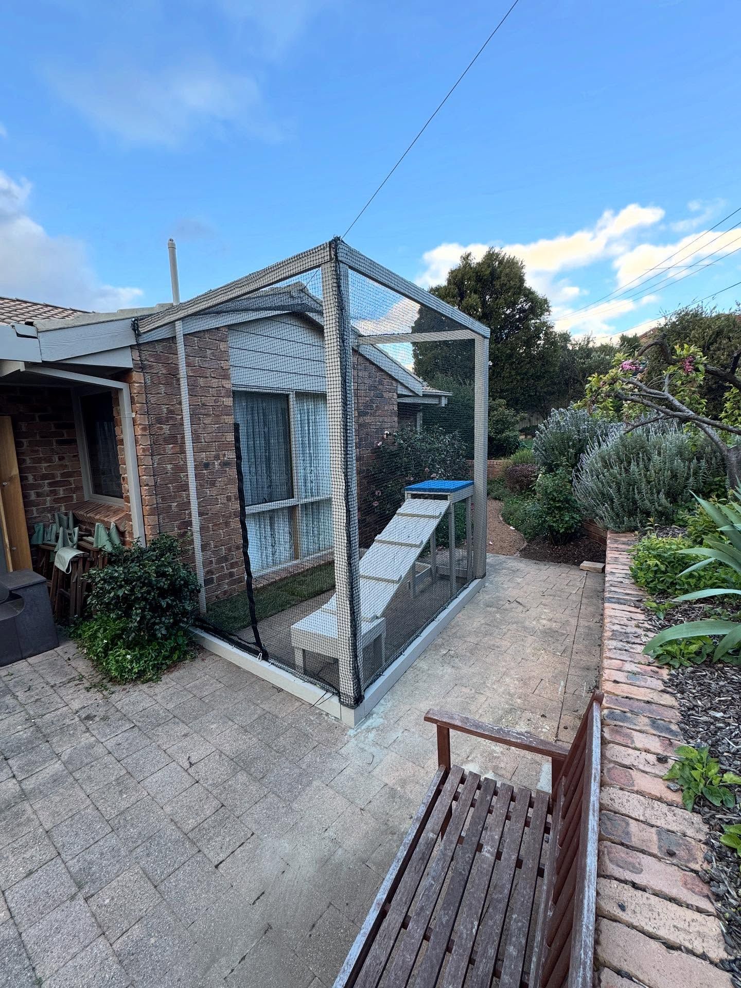 Backyard Patio With a Small Wire-enclosed Shed Beside a Brick House and a Bench in the Foreground. — Catios By Paulie in Blackbutt, NSW