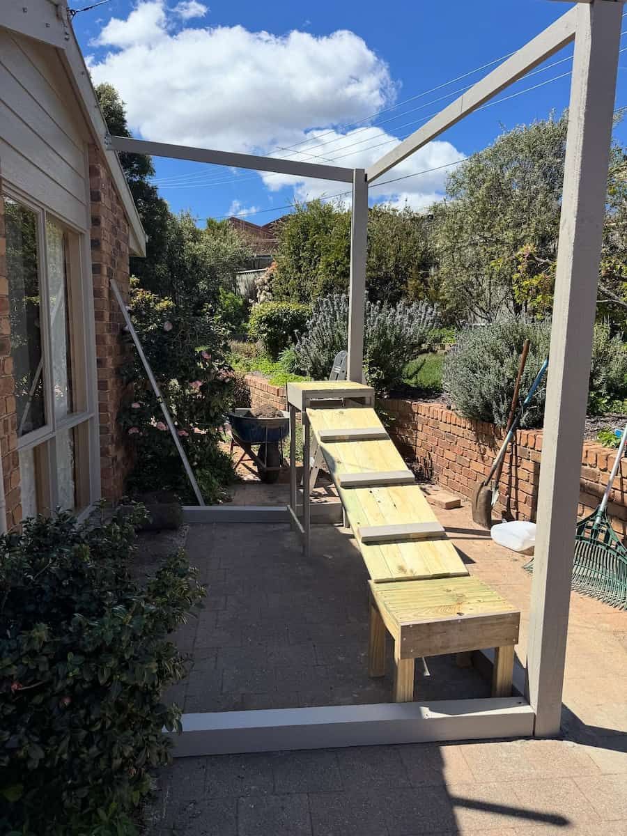 Garden Walkway With Wooden Benches and a White Pergola Beside a House — Catios By Paulie in Sydney, NSW