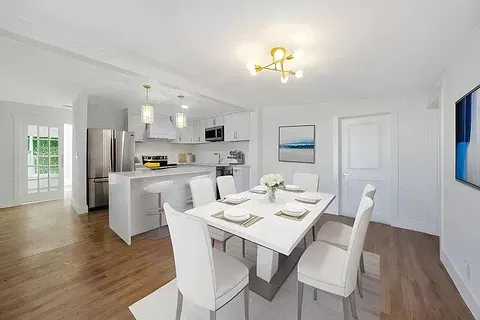 A dining room with a table and chairs and a kitchen in the background.