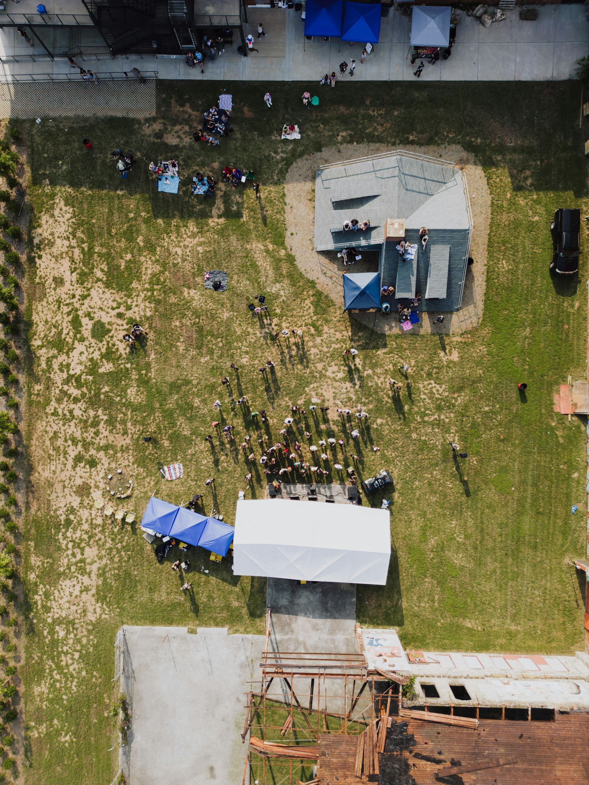 Aerial view of a grassy outdoor gathering with tents, a small building, and scattered people.