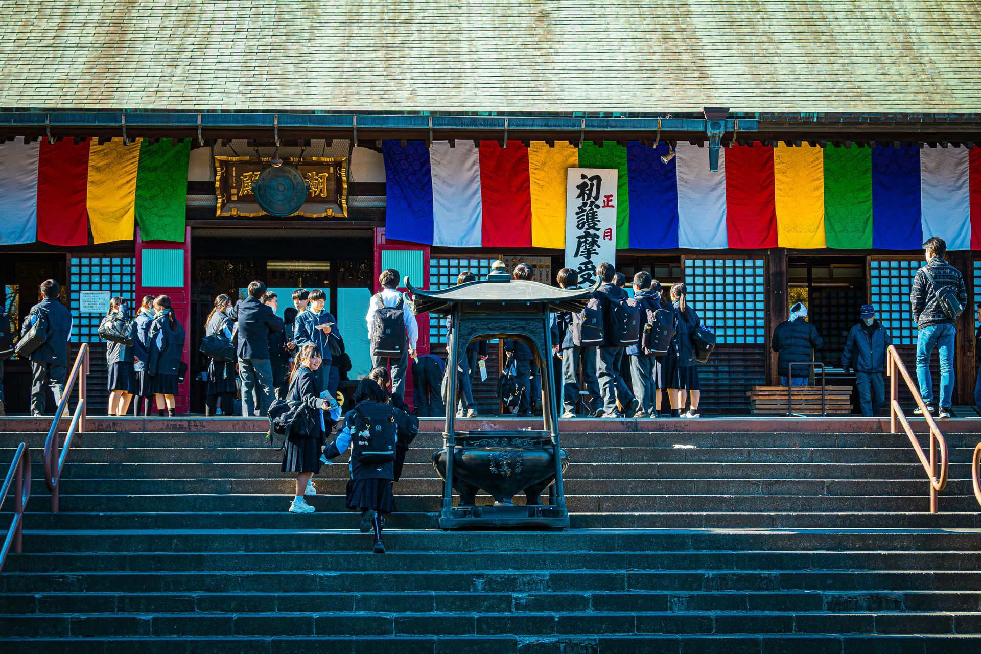 People gathered on steps outside a building with colorful hanging banners and blue doors.
