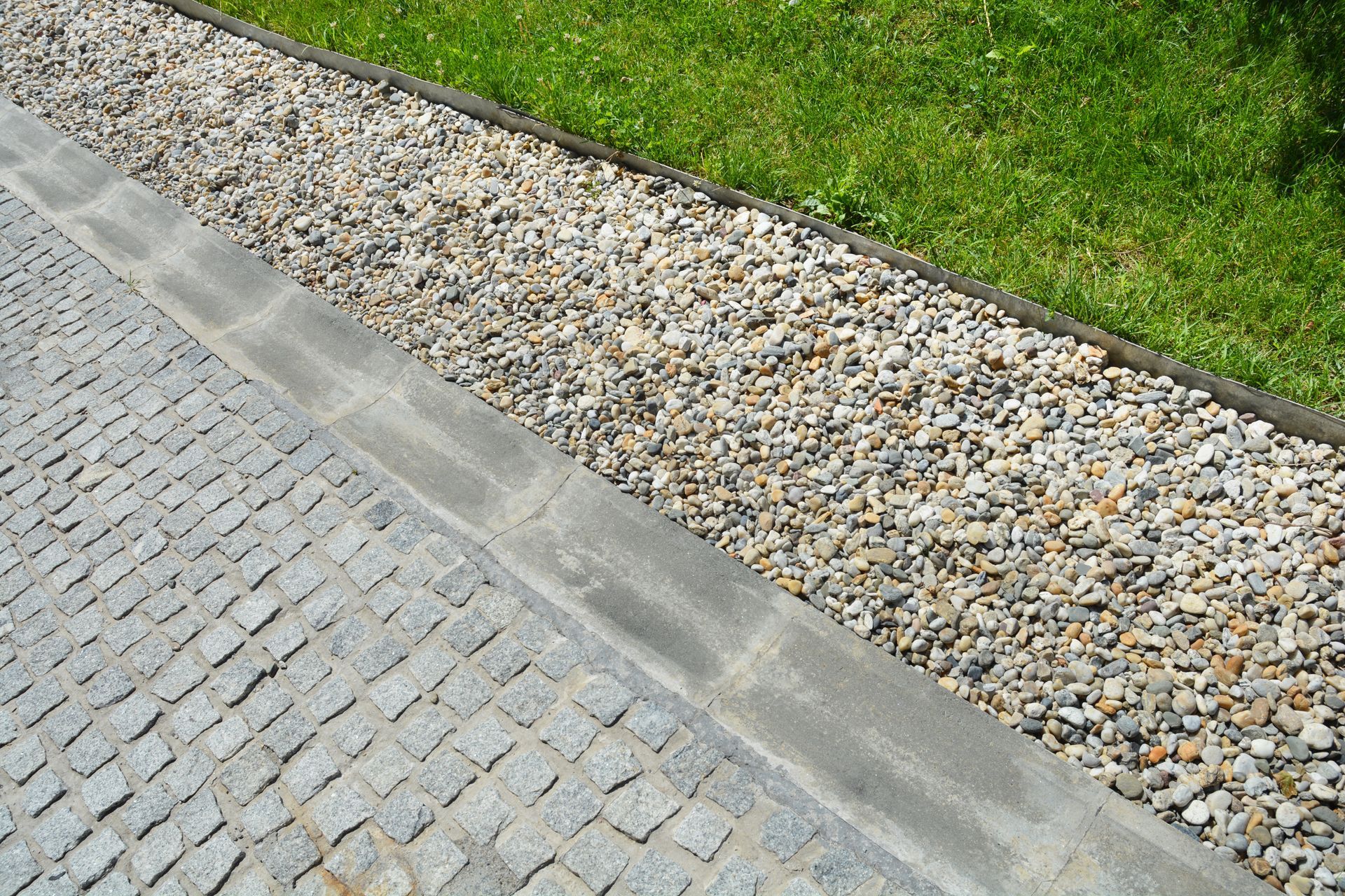 Gravel drainage bed beside stone pavement and grass lawn. Gravel drainage bed beside stone pavement and grass lawn.