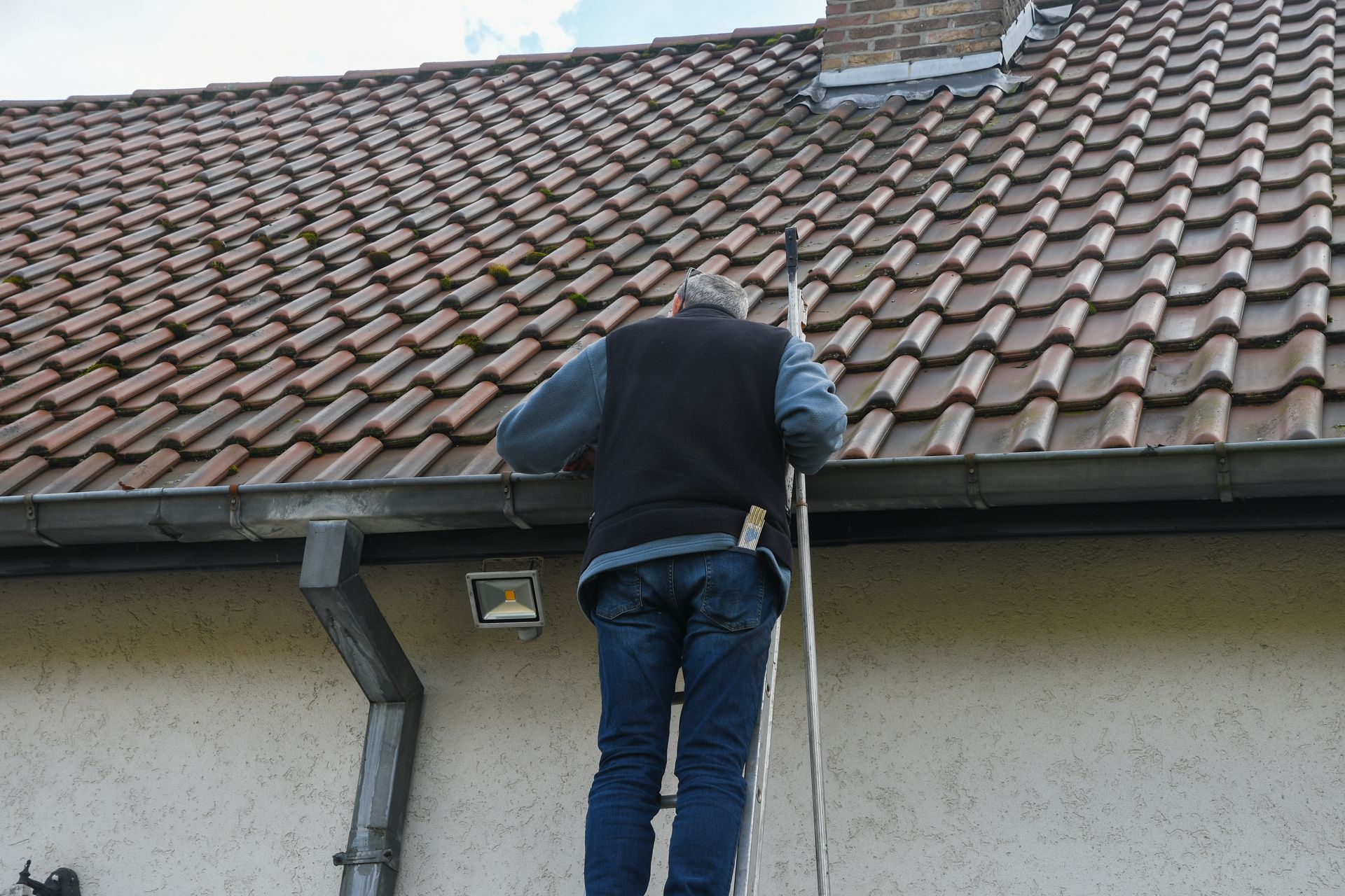 Professional roofer cleaning residential gutter while balancing on metal ladder. Professional roofer cleaning residential gutter while balancing on metal ladder.