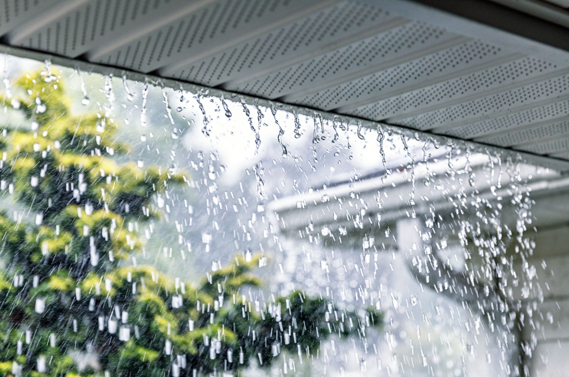 View of downpour rainstorm Water is over a roof and an aluminum rain gutter.