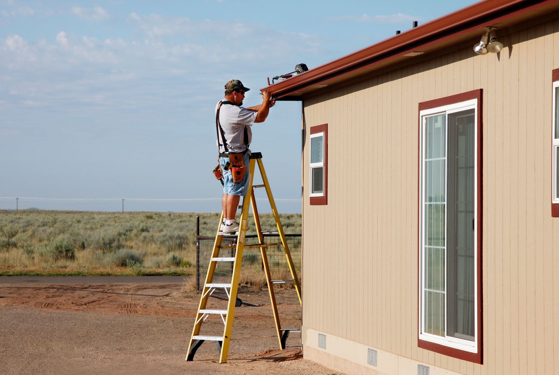 A male worker on a ladder is performing gutter installation, on a residential home.