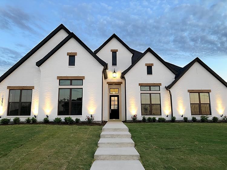 Modern white house with black trim, lit windows, and a front walkway at dusk