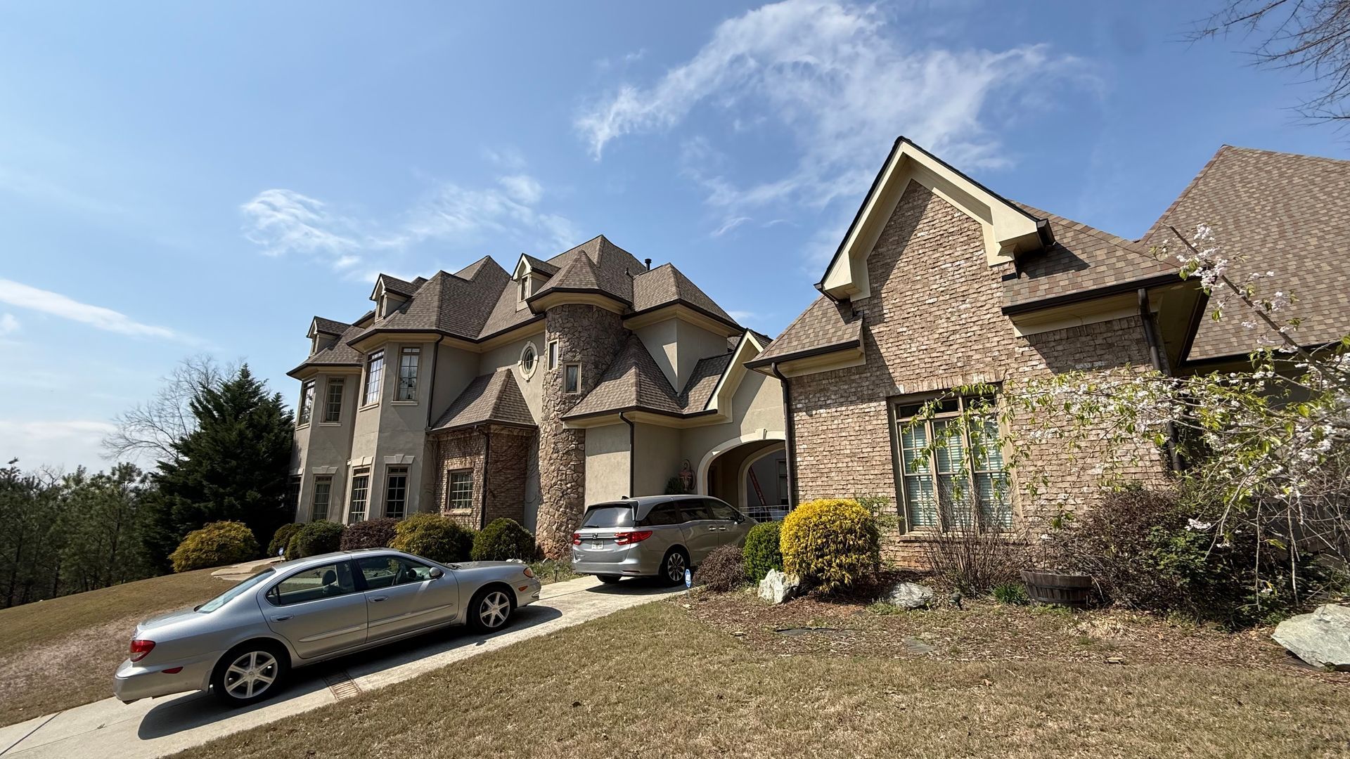Suburban stone house with parked cars and landscaped front yard under a blue sky