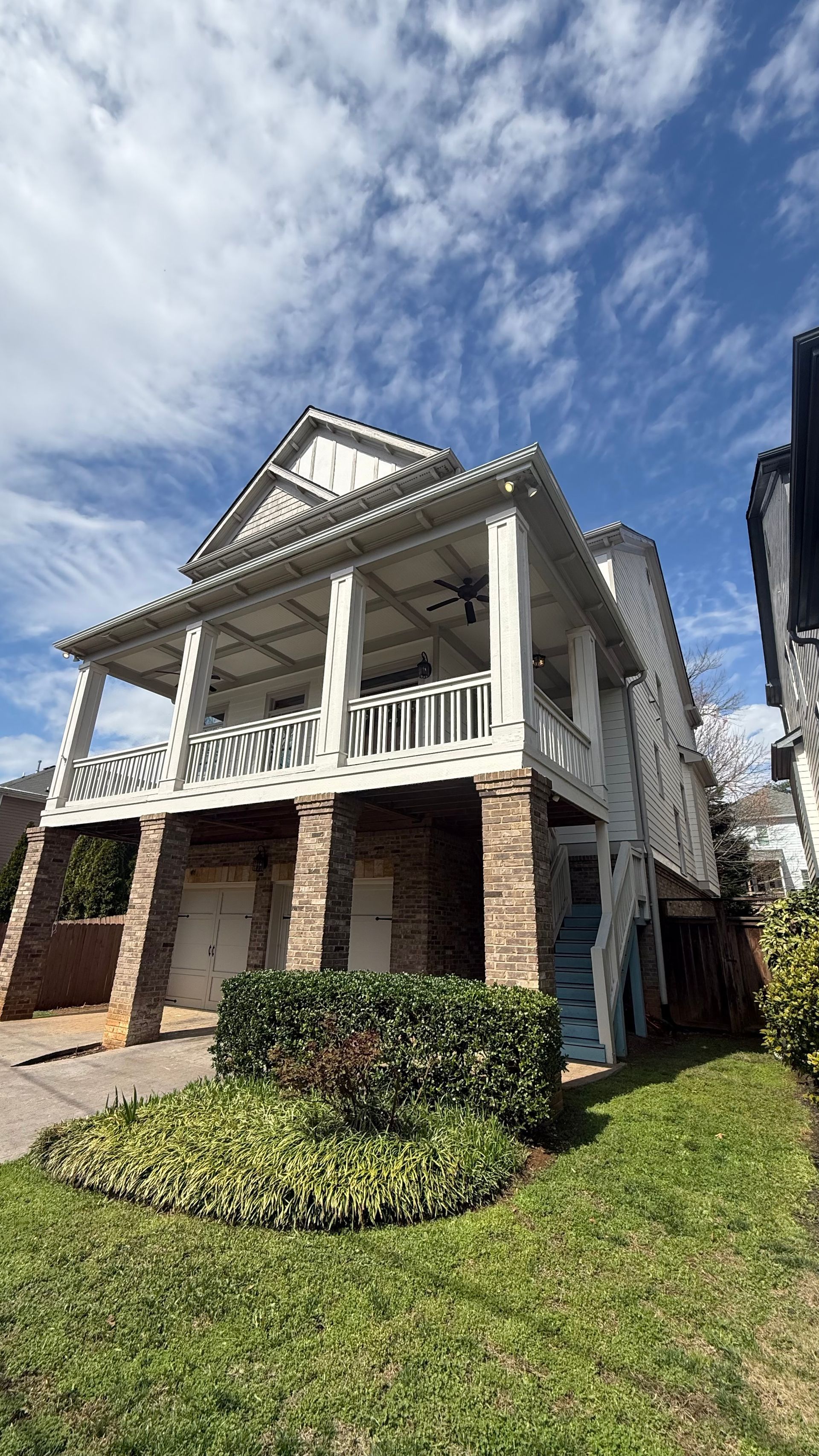 White two-story house with a front porch, brick lower level, and green lawn under a blue cloudy sky