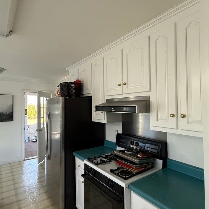 Bright kitchen with white cabinets, teal counters, black stove and fridge, and doorway to outside.