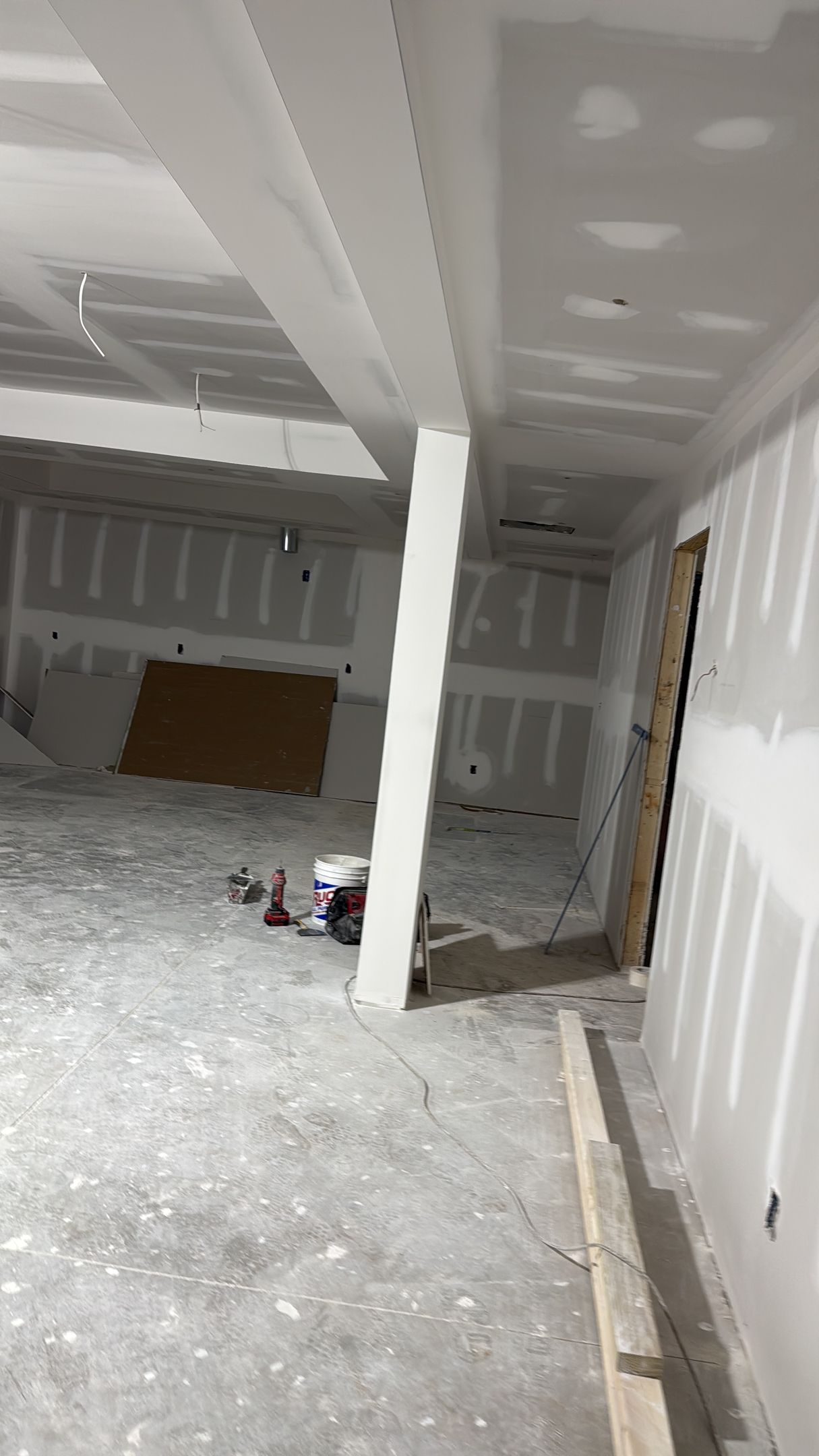Empty unfinished room with drywall, exposed ceiling beams, and construction debris on the floor