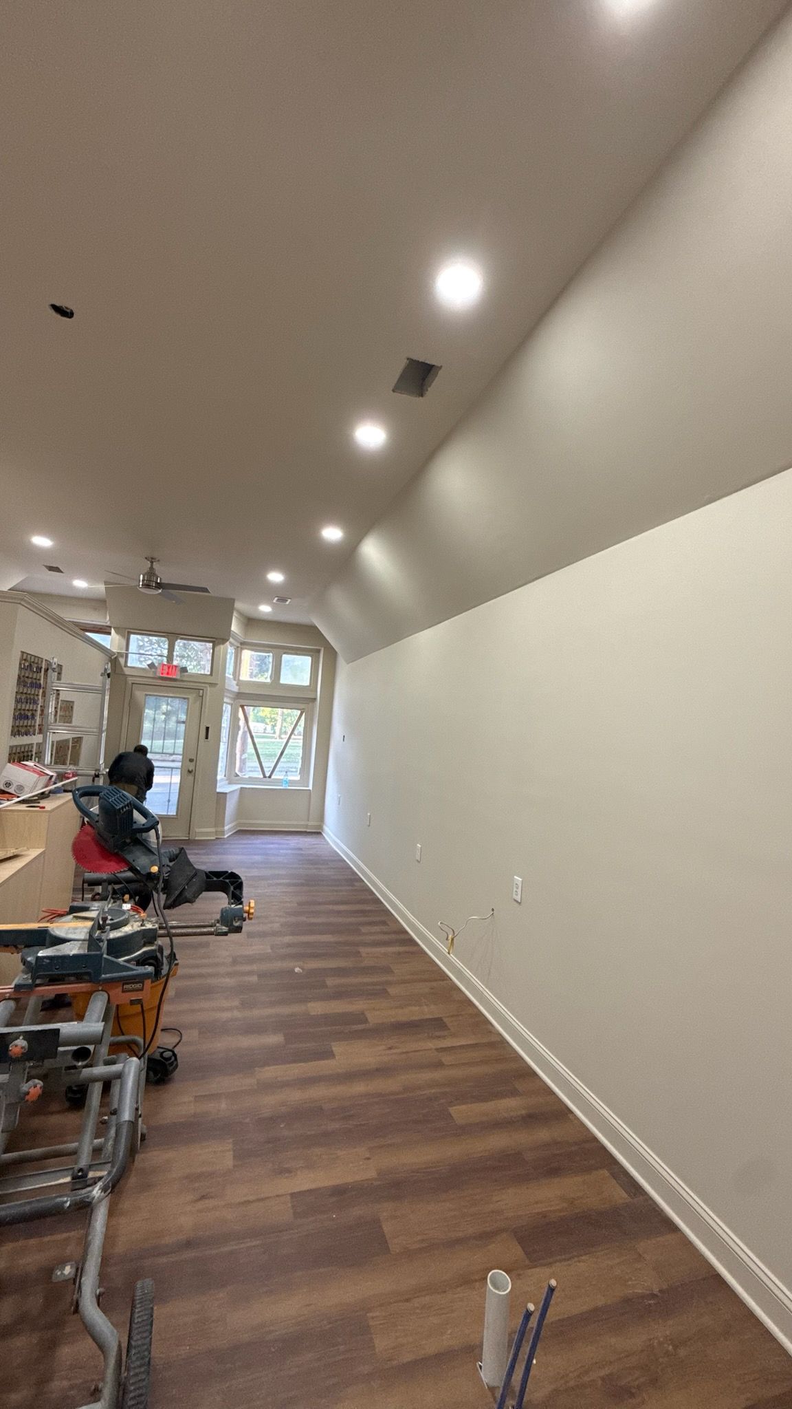 Long narrow hallway under construction with white walls, wood floor, and tools/materials along one side
