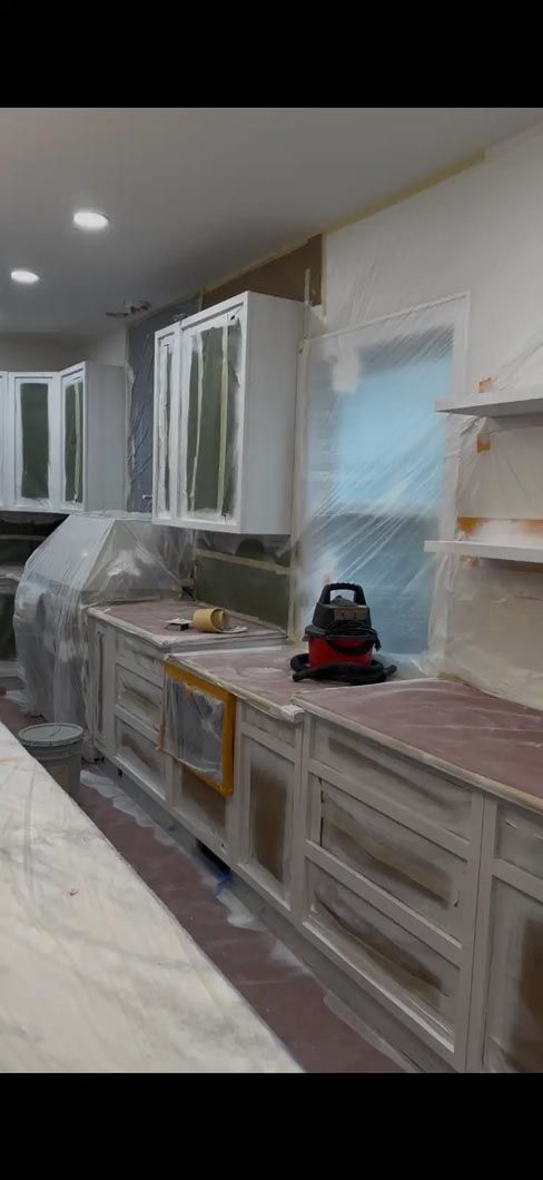 Kitchen under renovation with covered cabinets, plastic sheeting, and a countertop sander