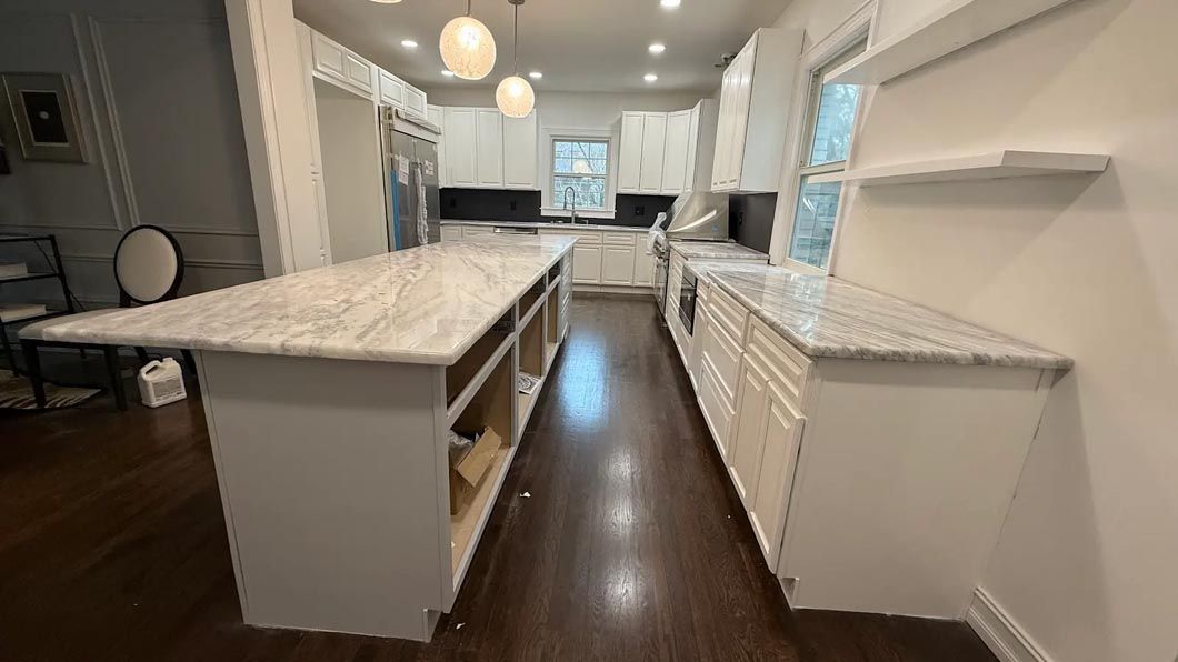 Bright modern kitchen with white cabinets, marble island, and dark wood floors