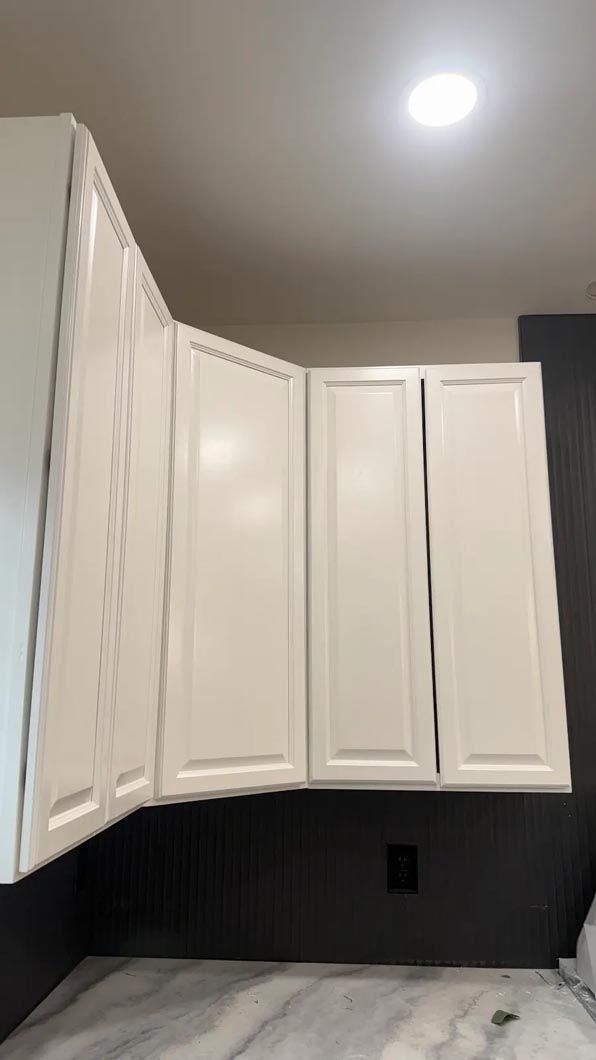 White kitchen cabinets under a ceiling light above a dark countertop and backsplash.