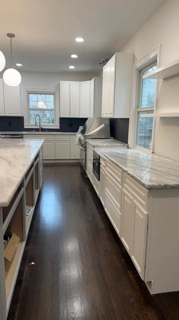 Bright narrow kitchen with white cabinets, gray countertops, dark wood floors, and stainless steel appliances.
