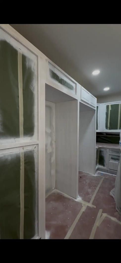 Hallway with green cabinet doors and white trim, partially covered for painting on a plastic-protected floor.