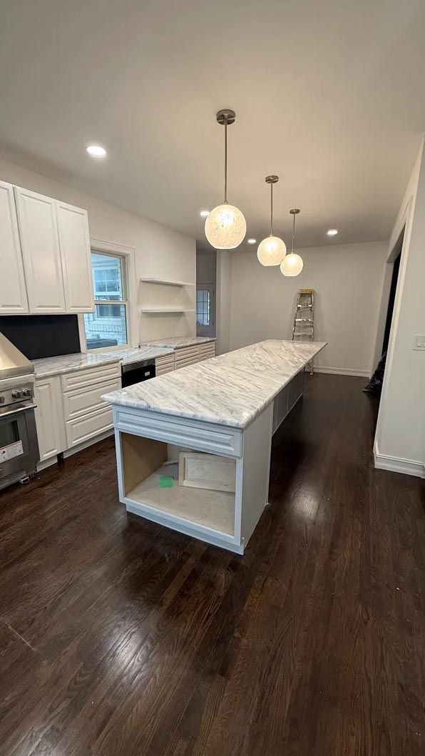Bright modern kitchen with marble island, pendant lights, white cabinets, and dark wood floors