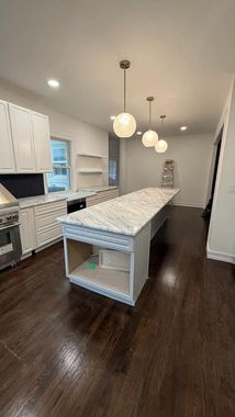 Bright modern kitchen with marble island, dark wood floors, white cabinets, and pendant lights.