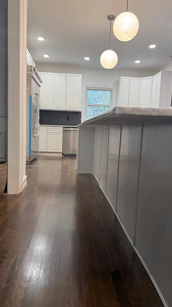 Modern kitchen with white cabinets, dark wood floors, pendant lights, and a large island