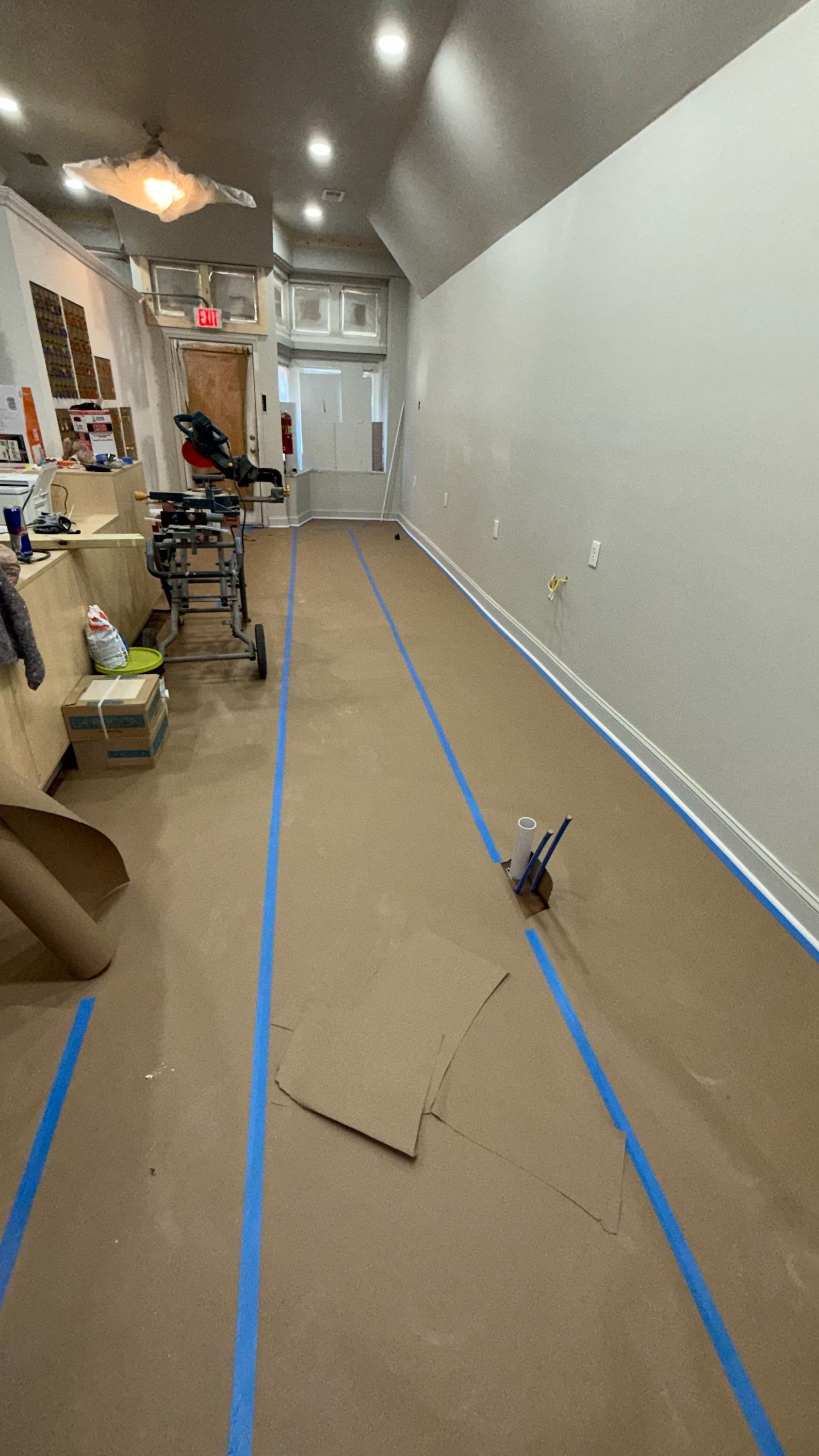 Narrow hallway with blue tape lines on the floor, scattered tools, and a doorway at the far end.