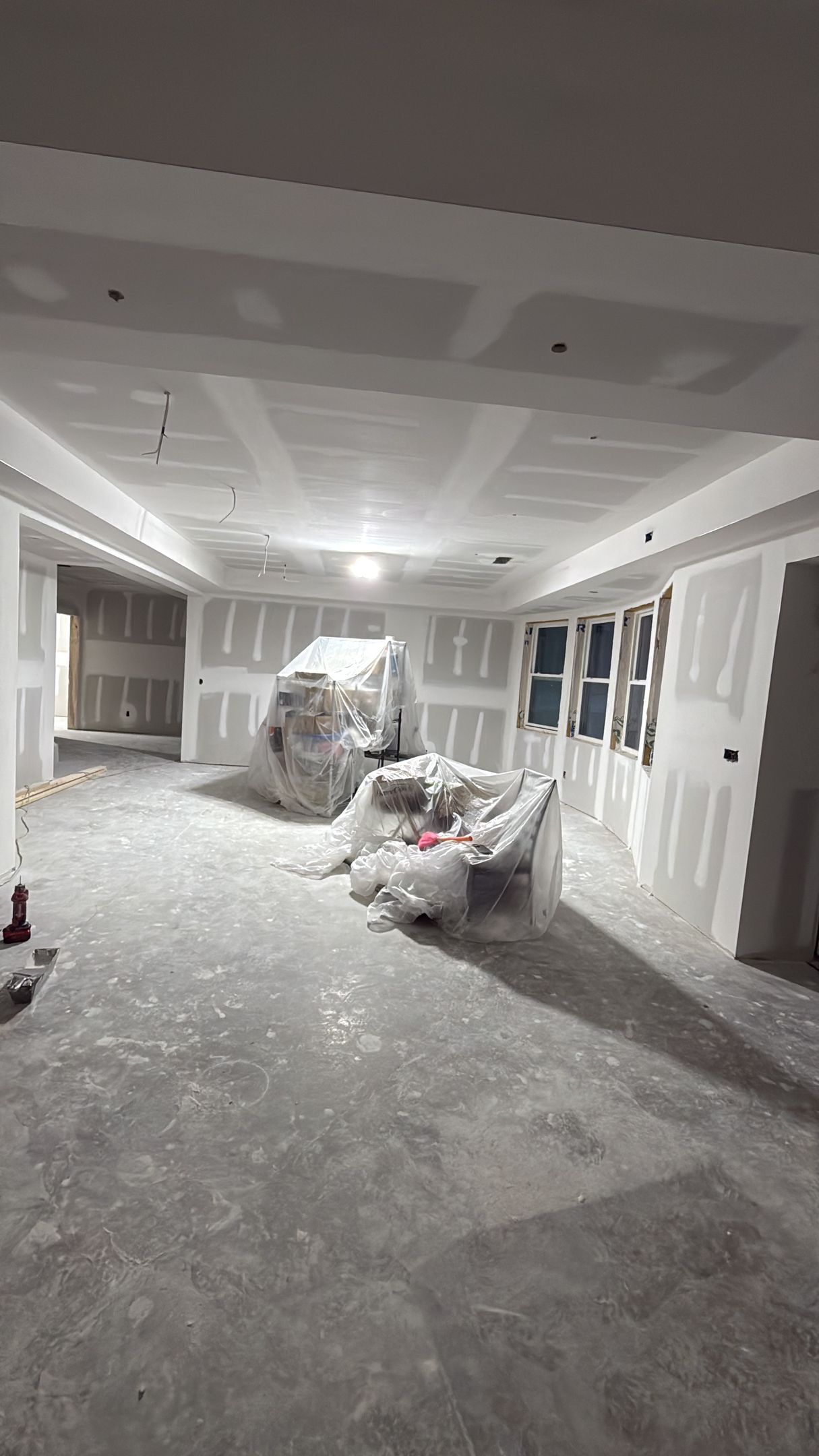 Renovation room with debris on the floor, covered furniture, and windows along the wall