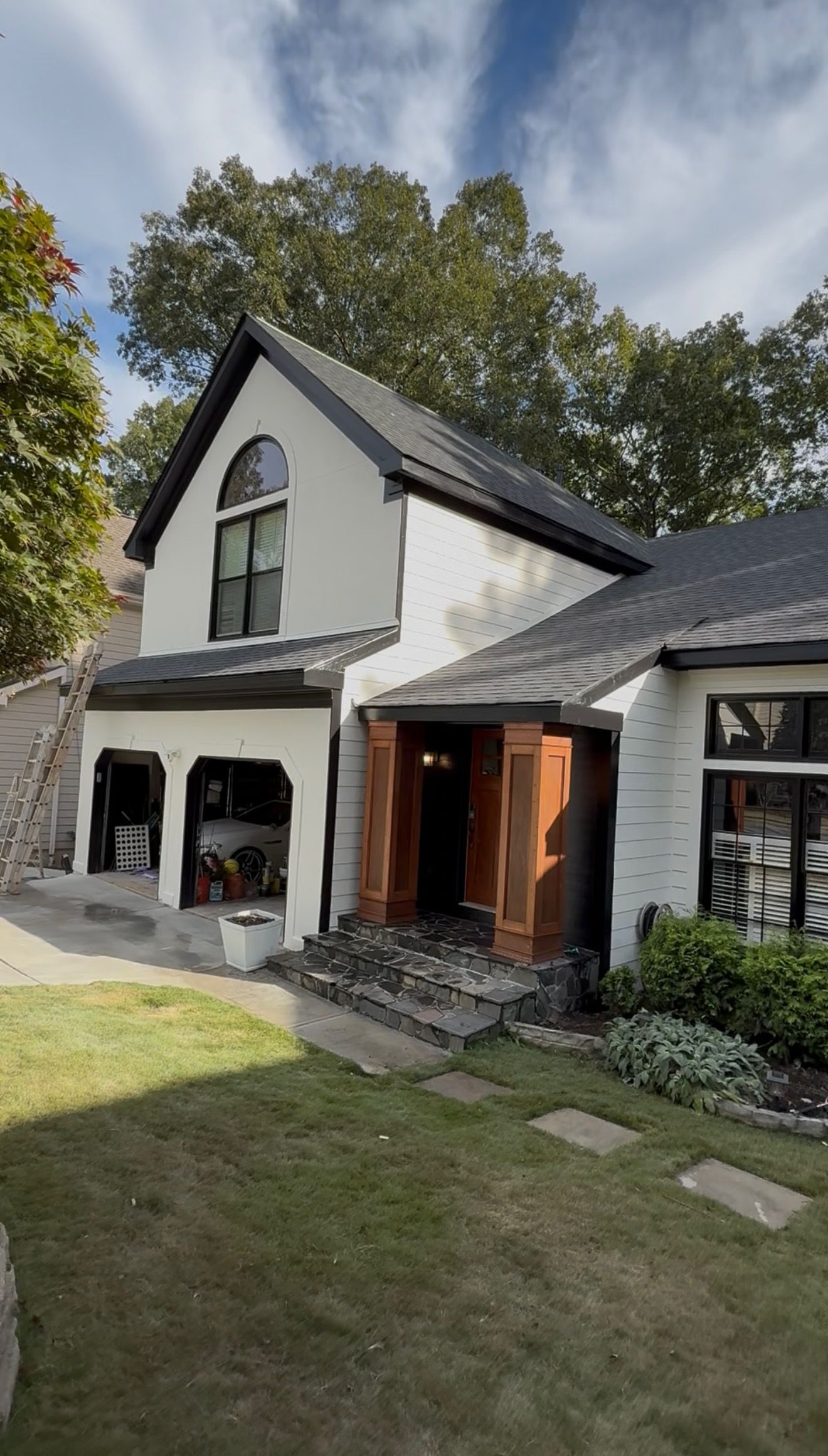 White cottage-style house with black roof, arched windows, front porch, and lawn under trees