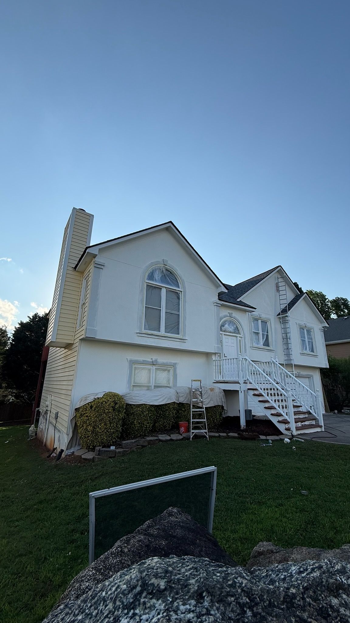 White house with stone chimney and front stairs on a grassy yard under a clear blue sky