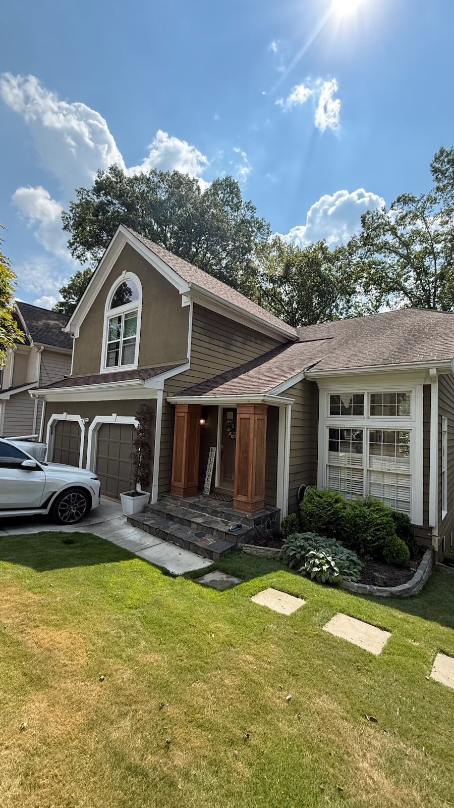 Suburban house with white car, green lawn, brick walkway, and bright blue sky