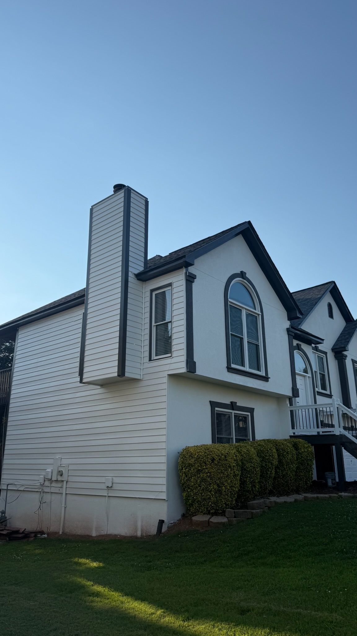 White townhouse with black trim and tall chimney beside a green lawn under a clear blue sky