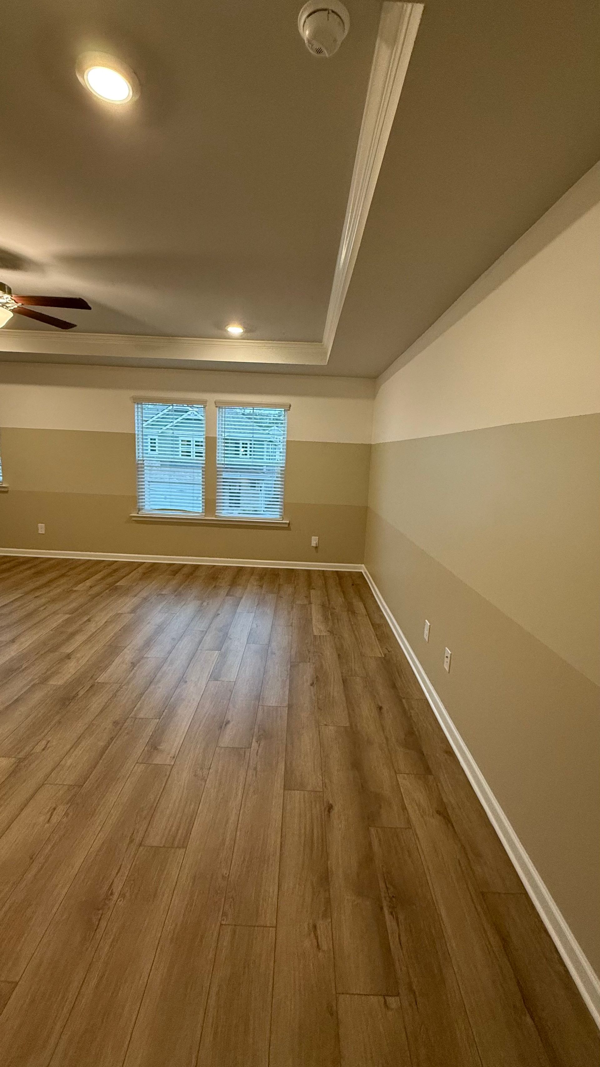 Empty room with wood floors, beige walls, a ceiling fan, and a window with blinds.