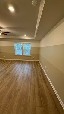 Empty beige room with wood floors, ceiling fan, and a small window with blinds.