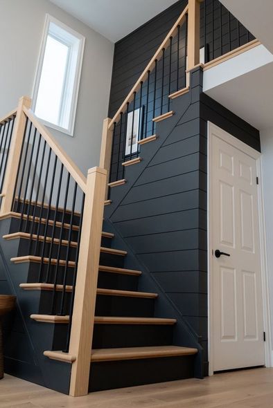 Modern staircase with dark blue accent wall, wood railings, and white door in a bright interior hallway