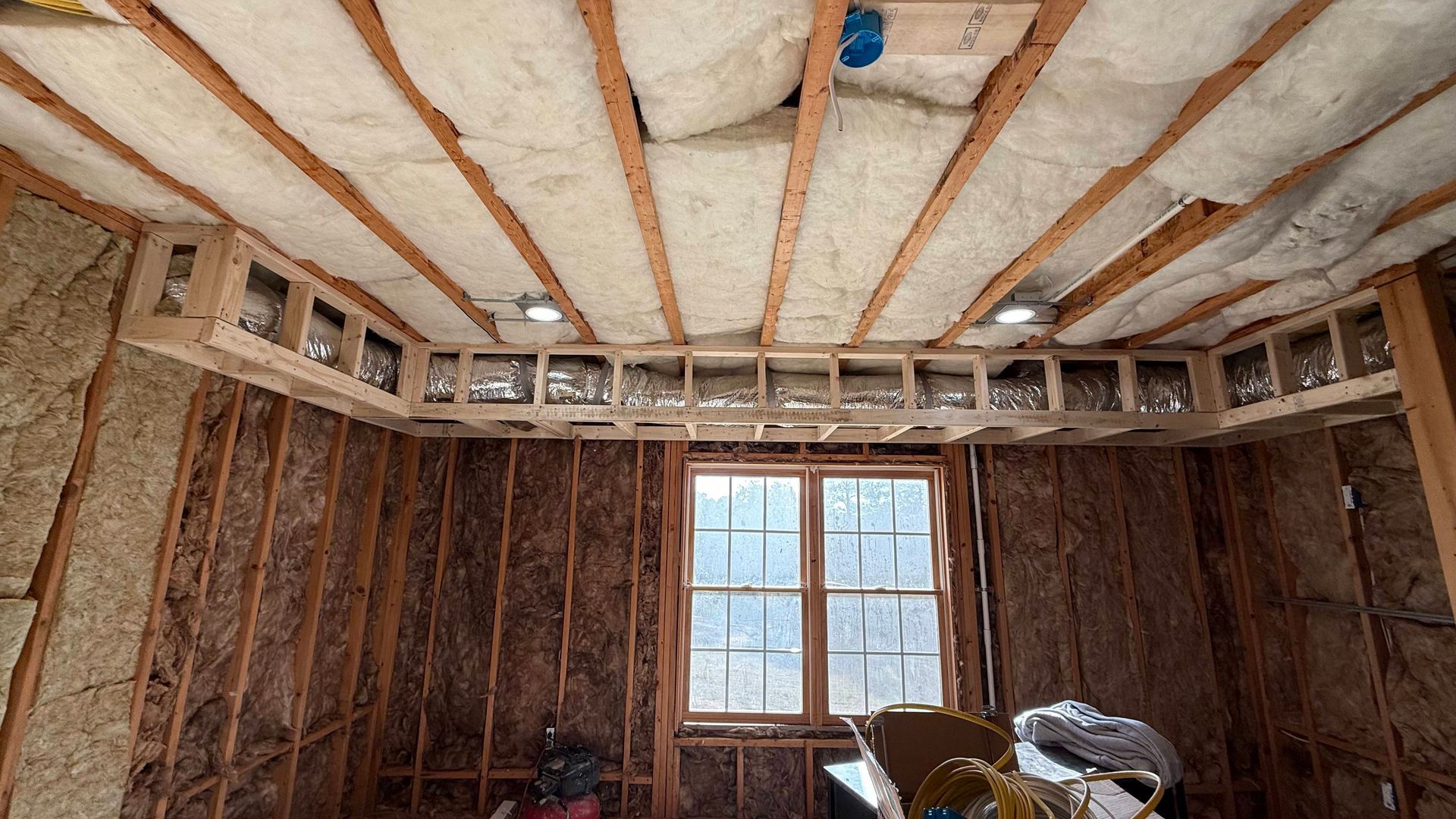 Unfinished room with exposed insulation and framing, small window centered on the far wall.