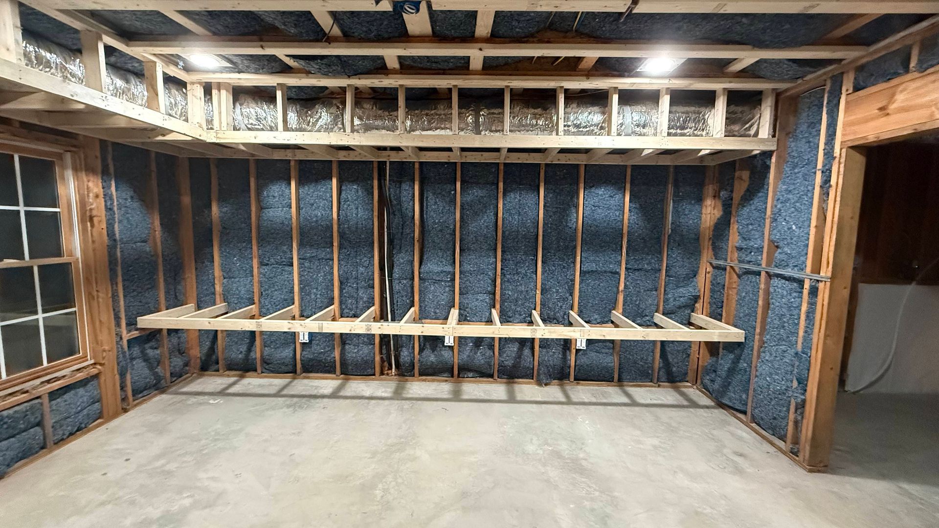 Bare basement room with exposed framing, insulated walls, and a long wooden workbench on sawhorses.
