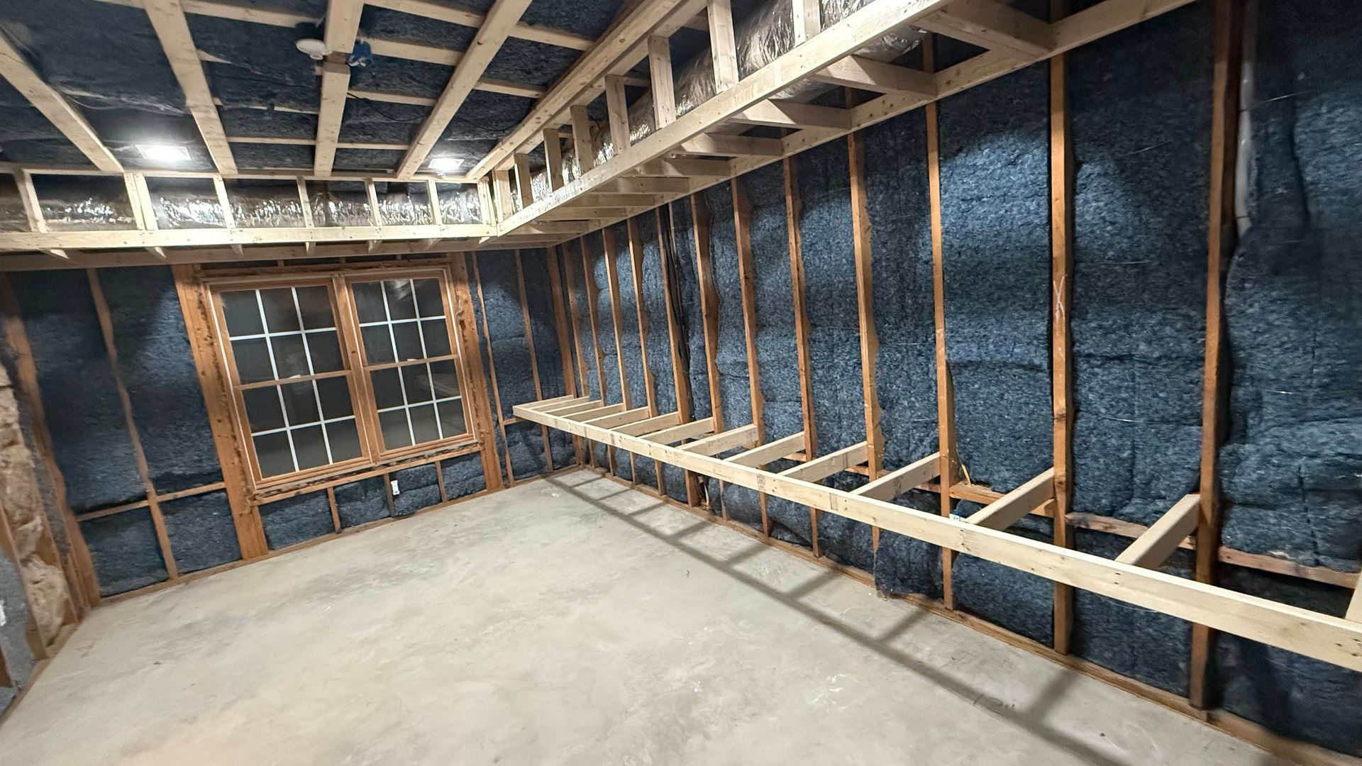 Unfinished basement framed with exposed wooden studs, insulated walls, and a concrete floor.