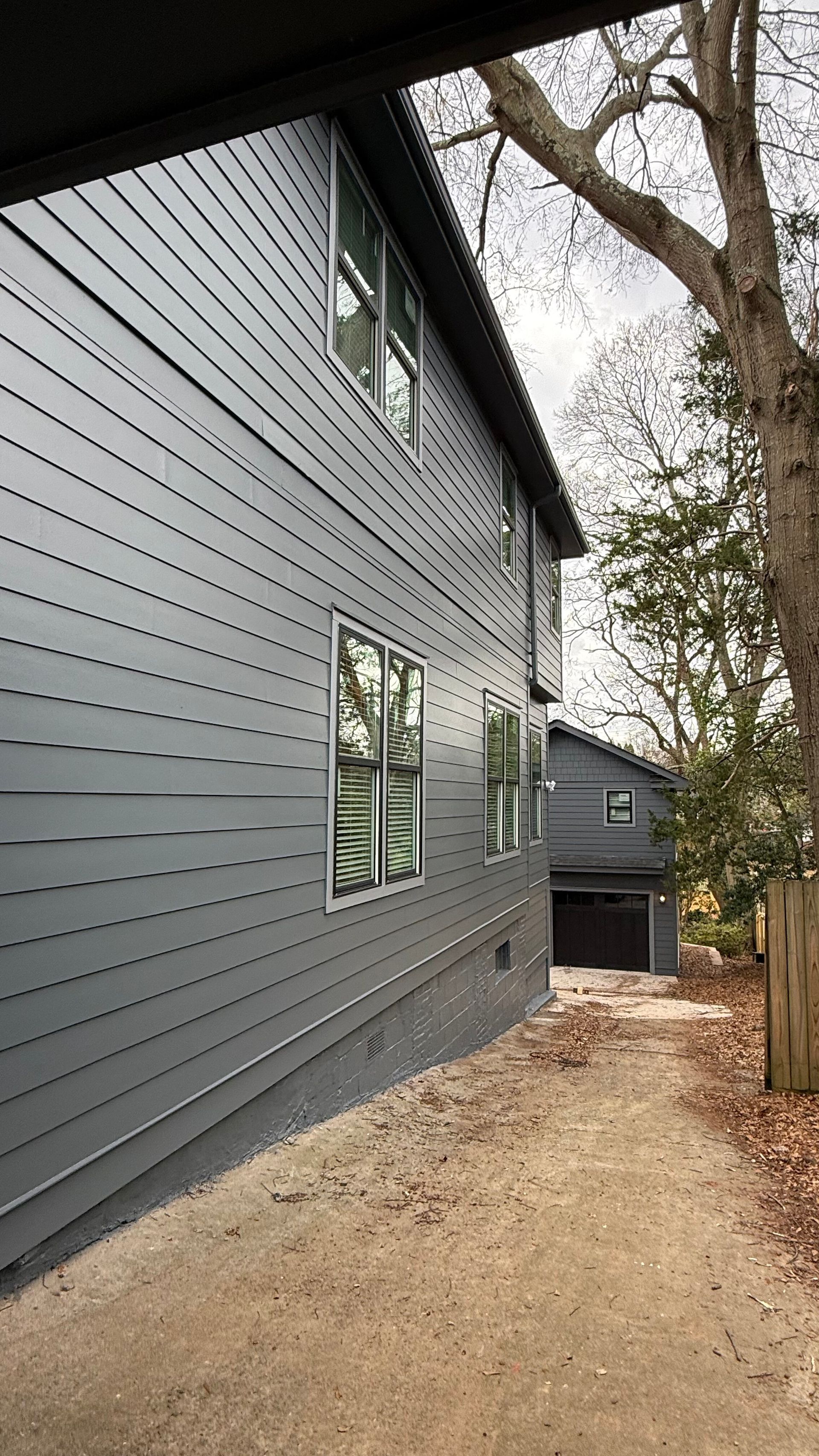 Gray house exterior with modern windows and a narrow dirt path beside trees