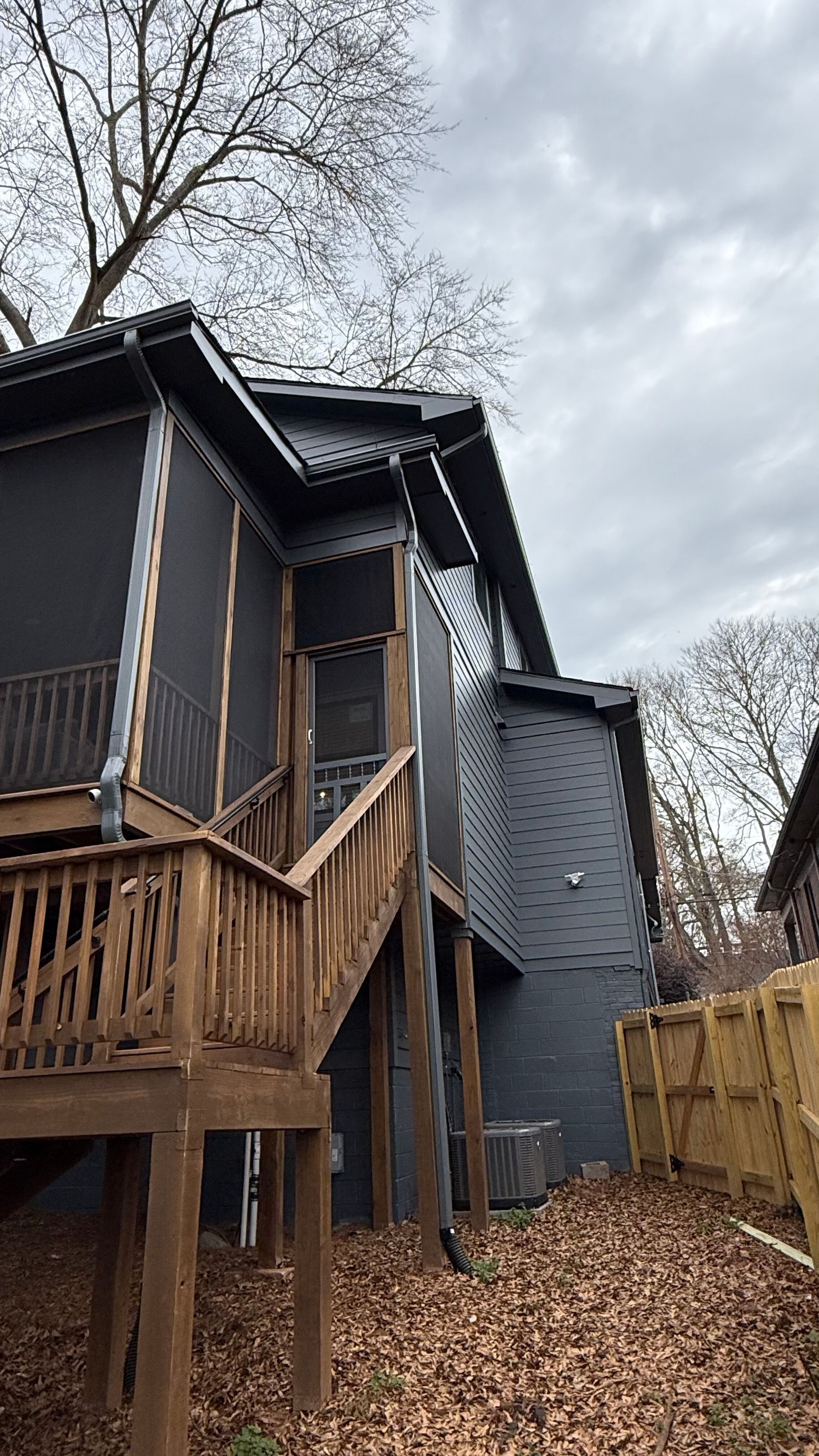 Side view of a dark house with wooden stairs and leaf-covered ground under a cloudy sky
