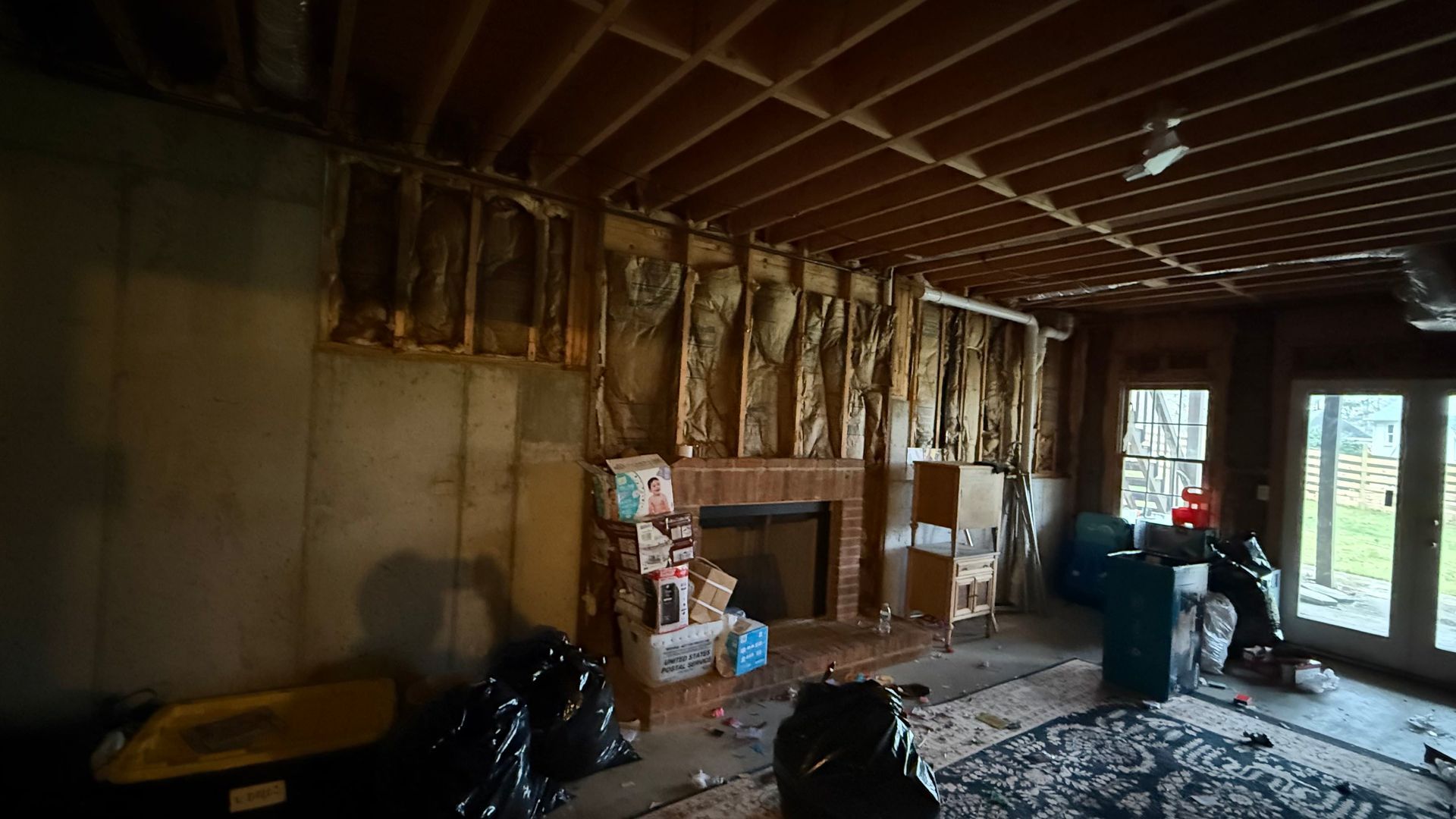 Unfinished room with exposed insulation, scattered debris, and a person near glass doors.