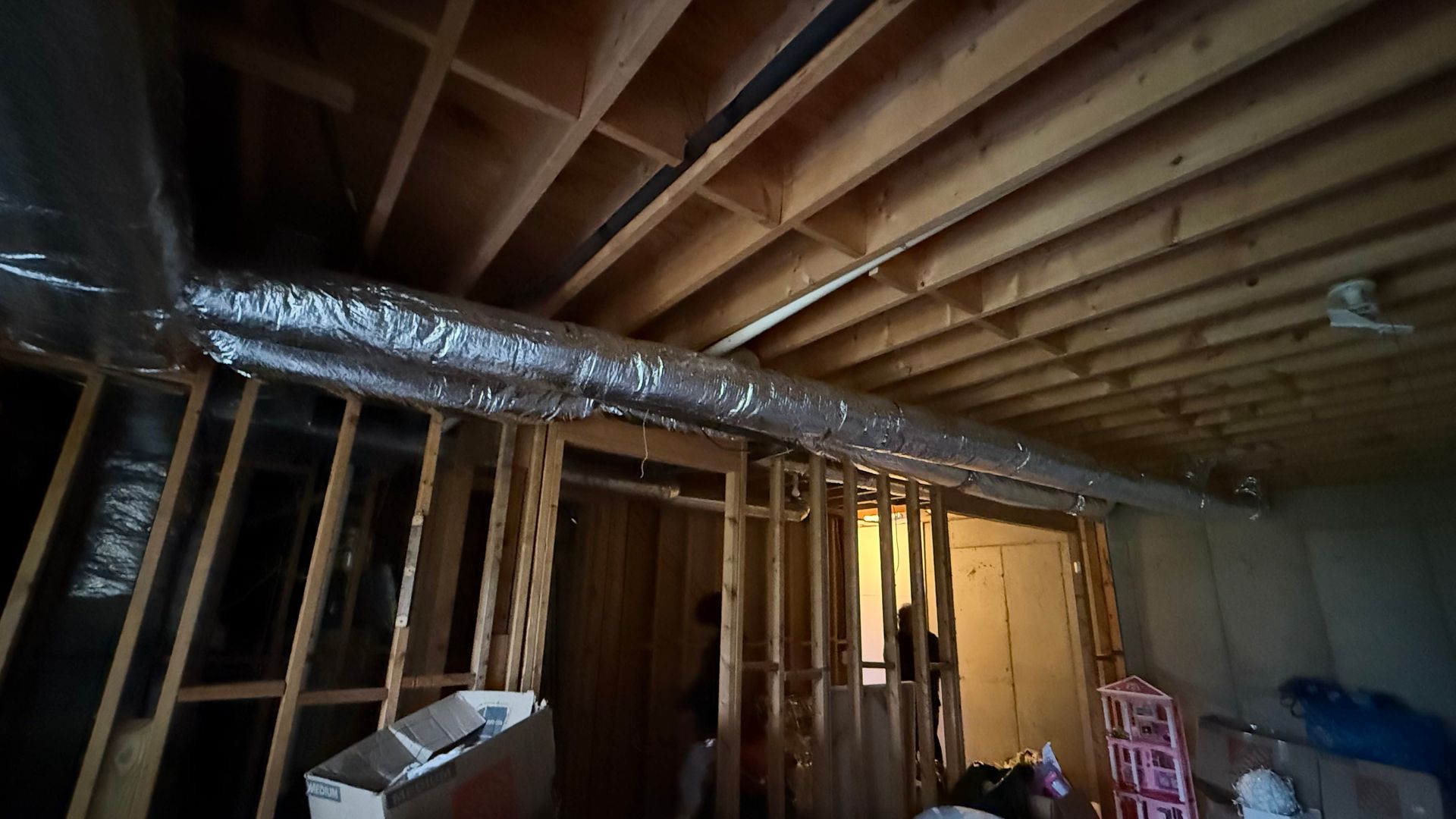Interior of a house under renovation with exposed studs, ductwork, and unfinished ceiling framing