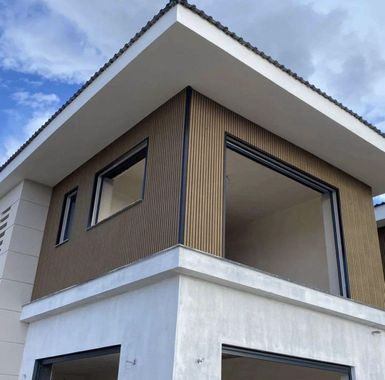 Modern house corner with white roof overhang, wood-paneled upper walls, and open balcony detail