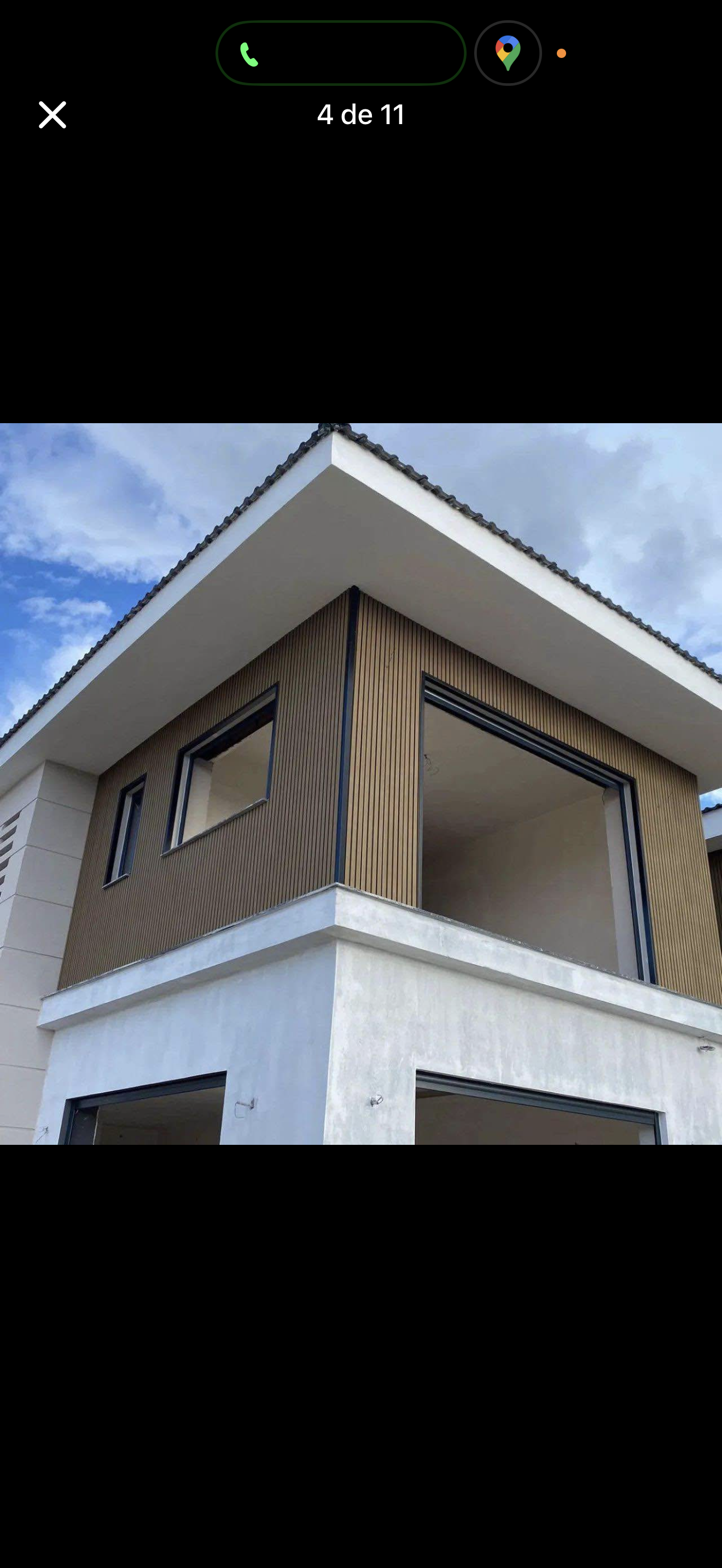 Two-story modern house exterior with white walls, wood paneling, and a gray roof against a blue sky