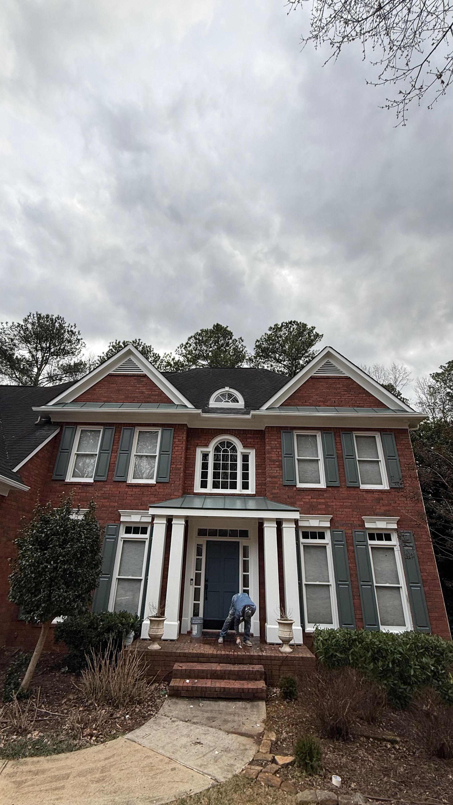 Two-story red brick house with white trim, front porch, and a cloudy sky above
