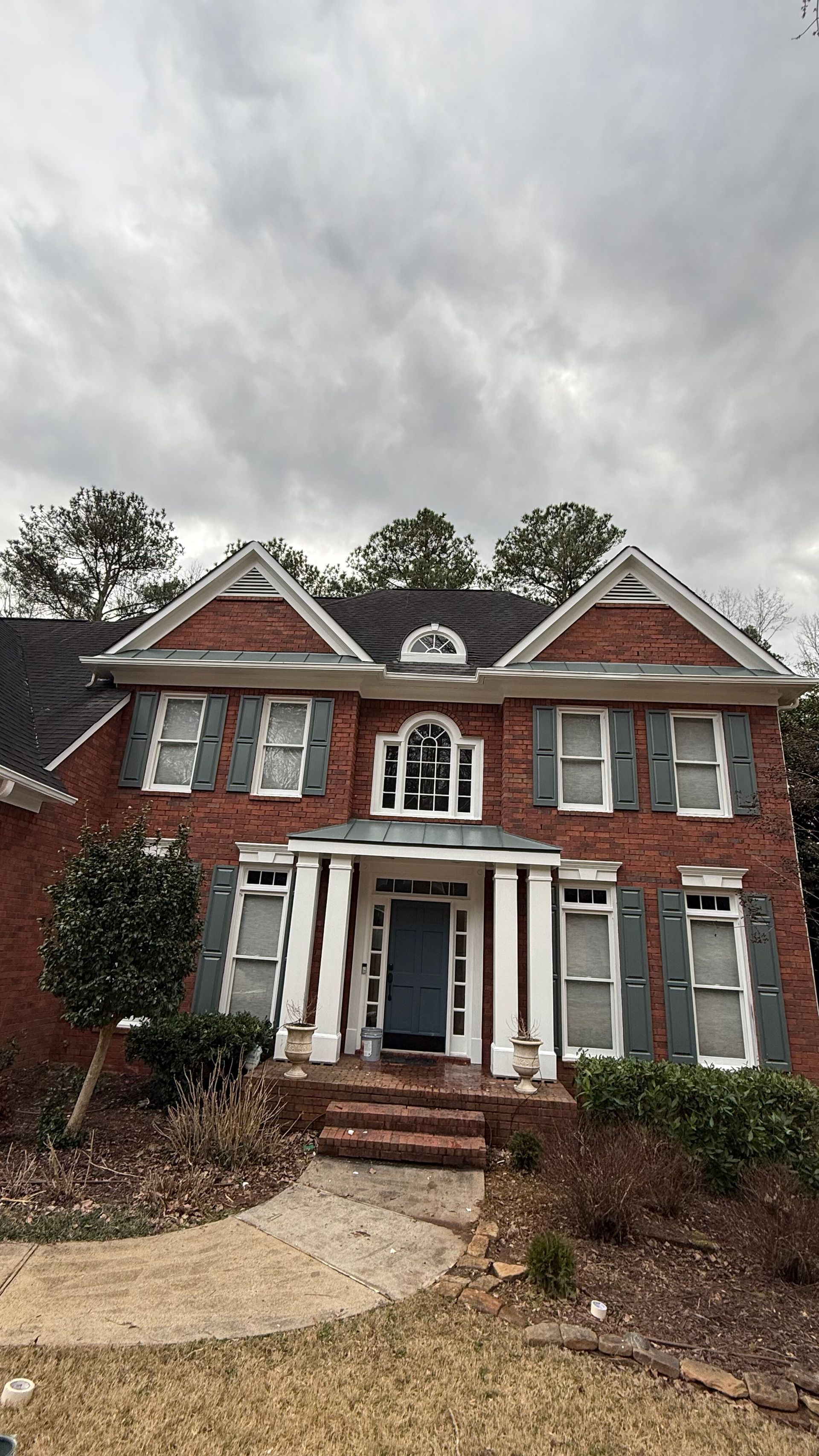 Red-brick two-story house with white trim, front porch, and cloudy sky above a gravel driveway