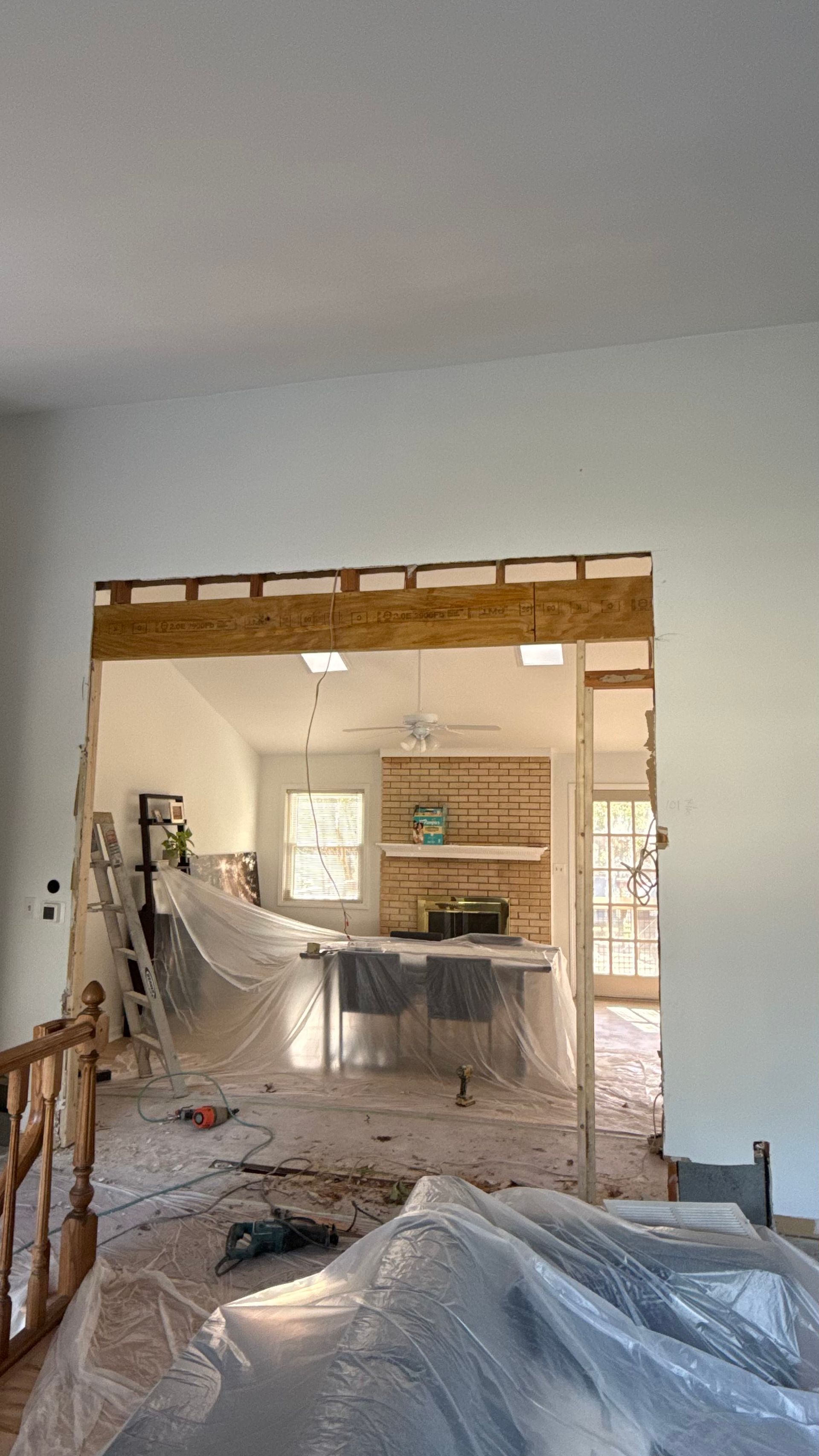 Partially demolished room with exposed framing, debris on the floor, and plastic sheeting during renovation