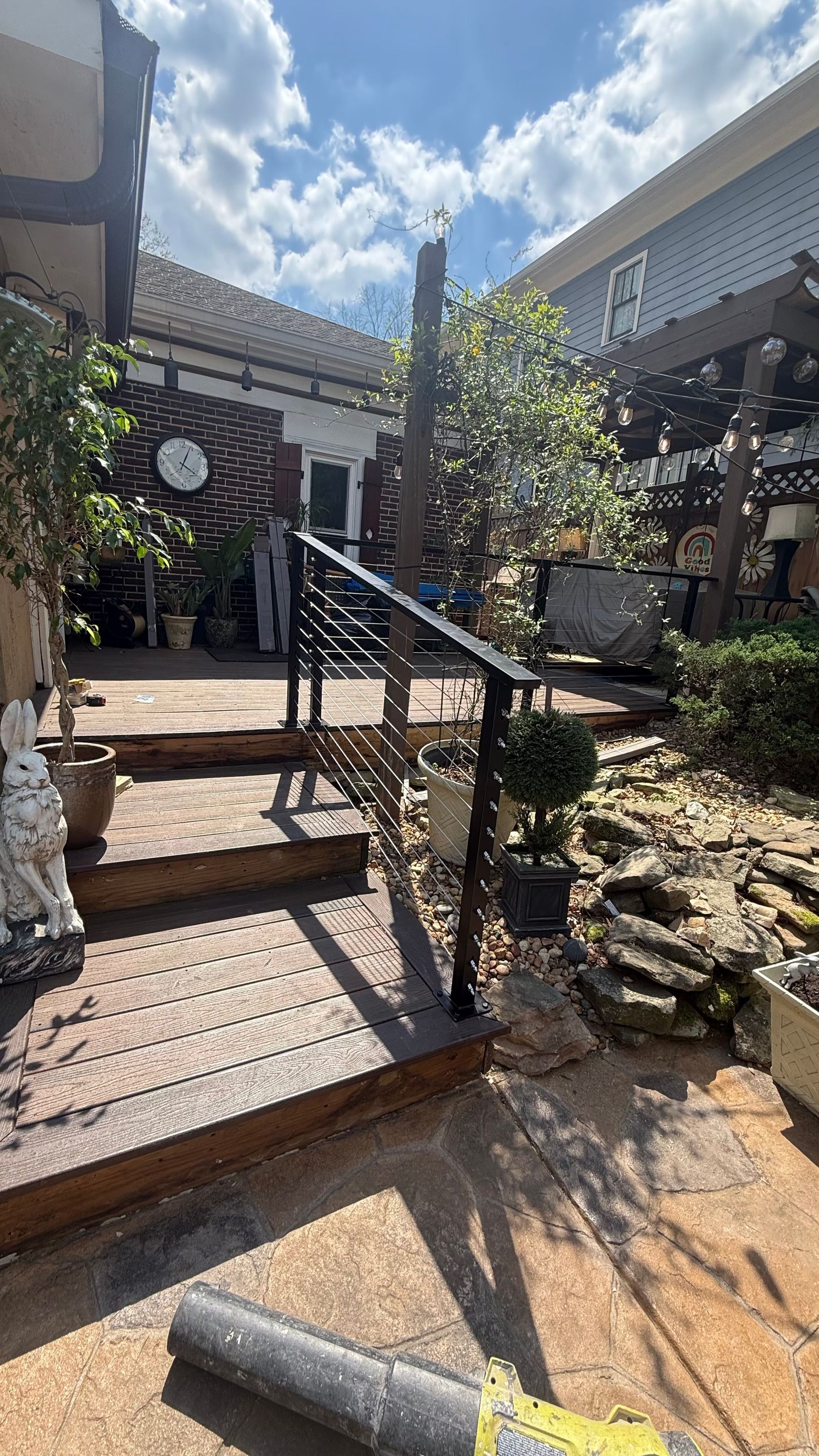 Front steps with metal handrails leading to a house entrance, bordered by plants and a rocky garden path.