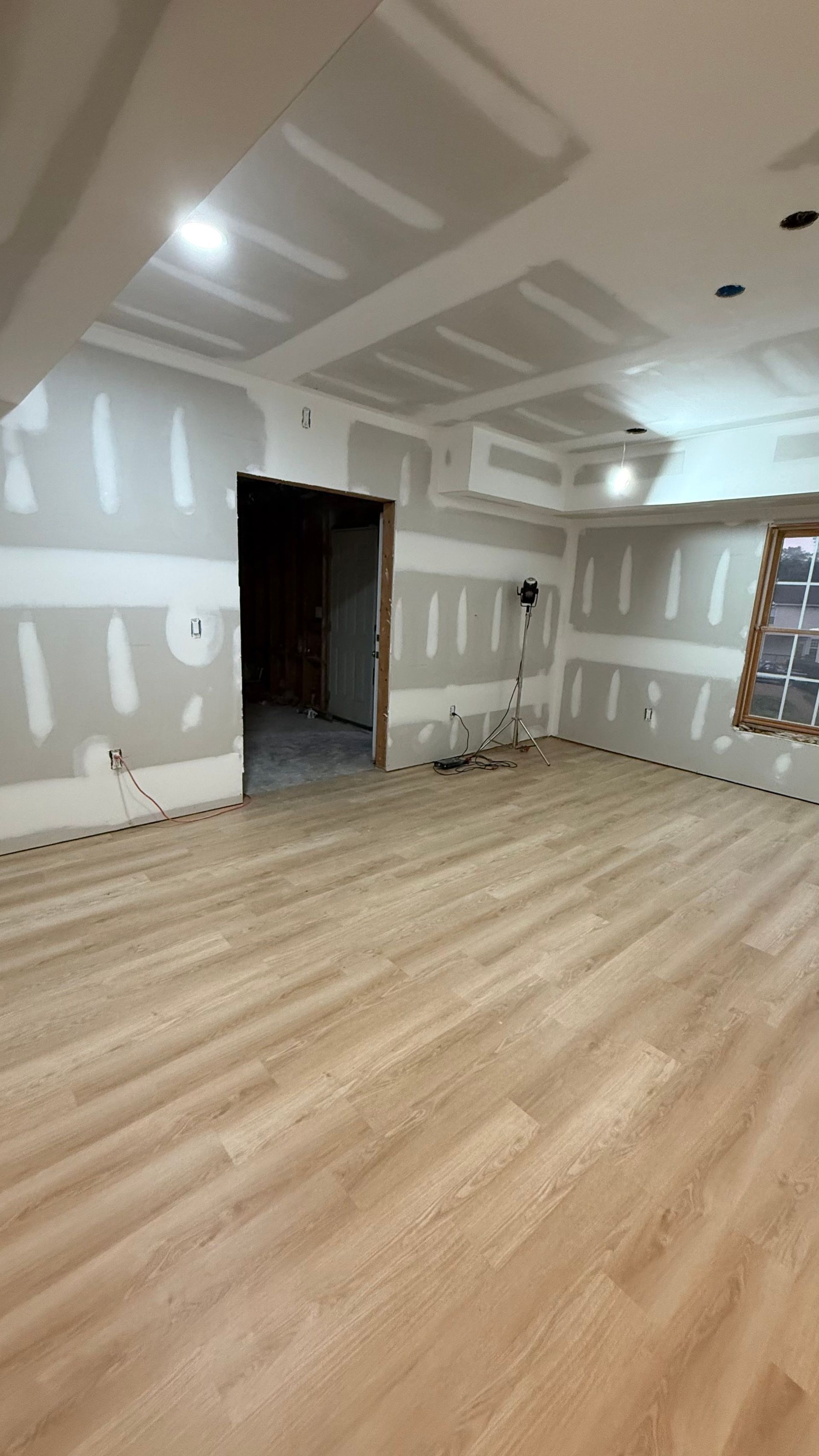 Empty unfinished room with light wood flooring, white drywall, and ceiling patchwork in progress.