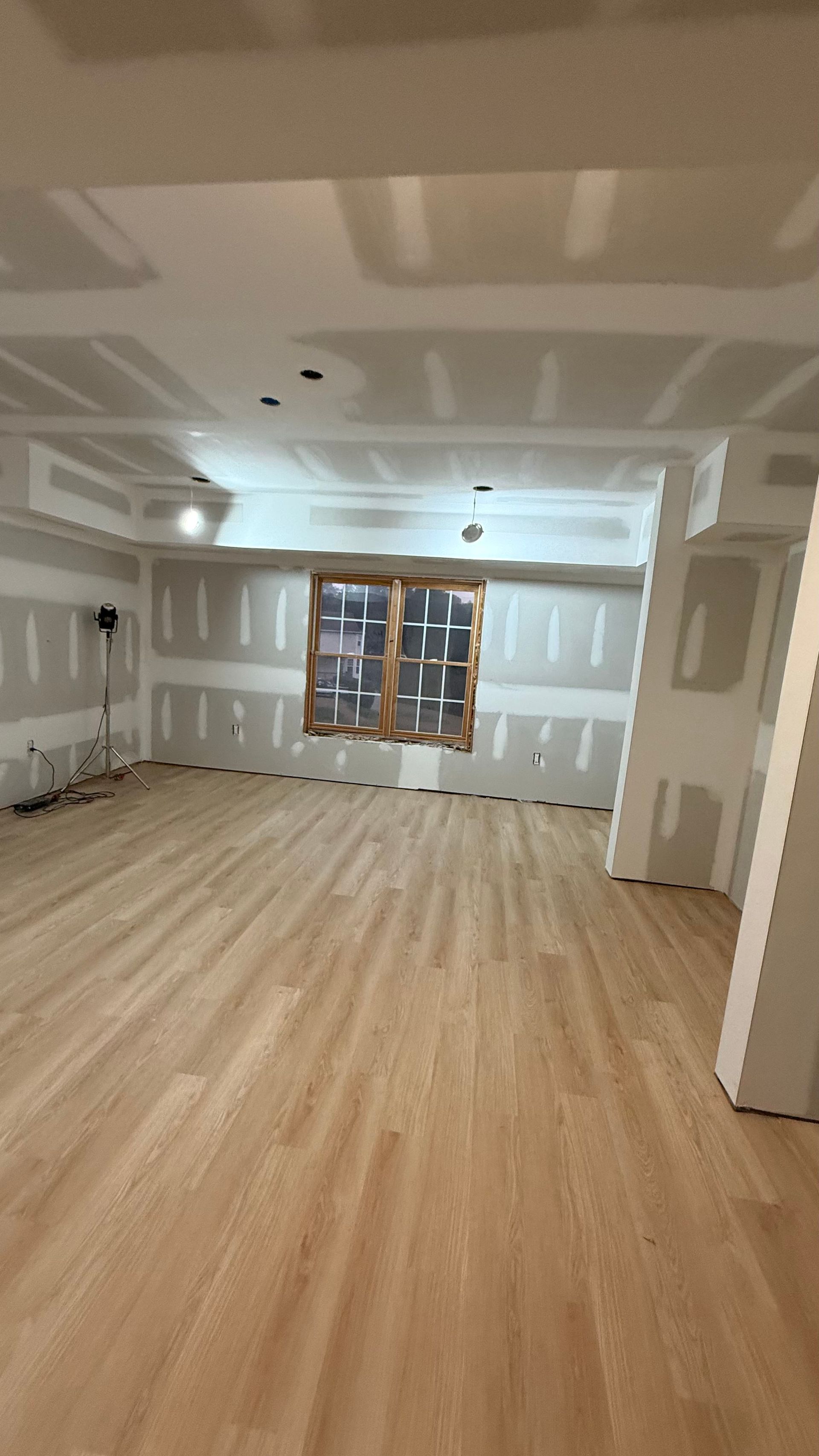 Empty unfinished room with drywall, wood flooring, and a window at the far wall.