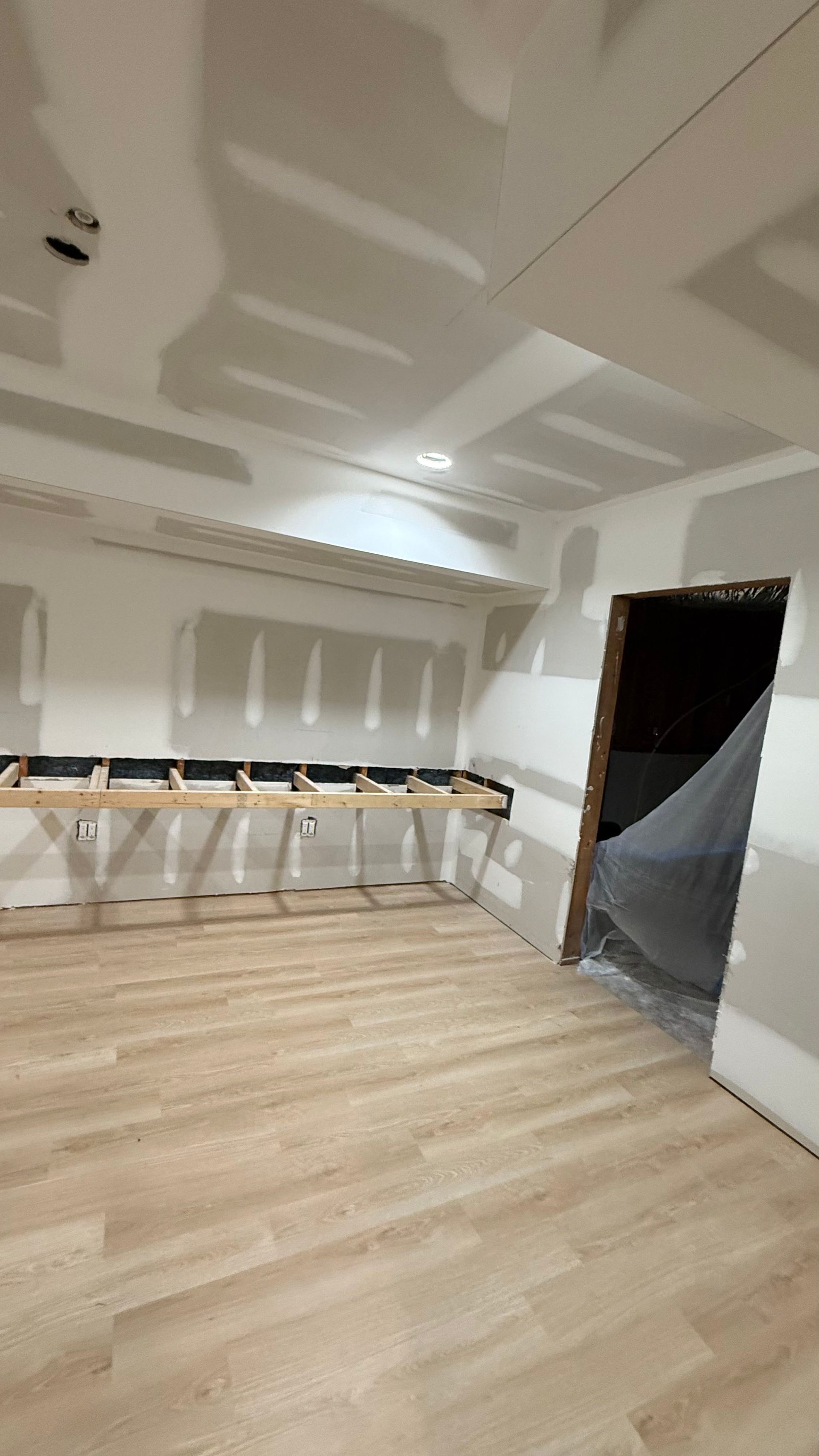 Empty room under renovation with wood floor, folding tables, and a doorway covered in plastic sheeting
