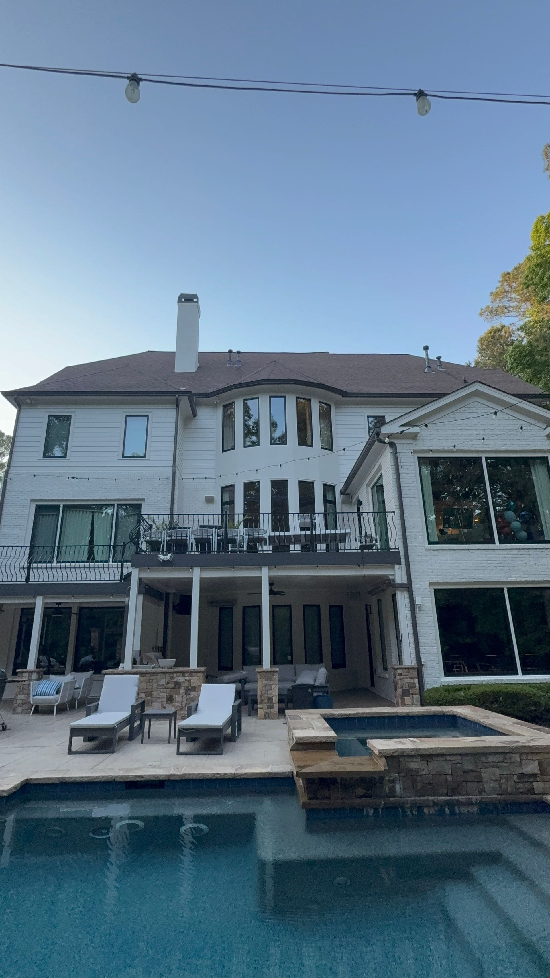 Backyard pool with lounge chairs in front of a large two-story white house and patio